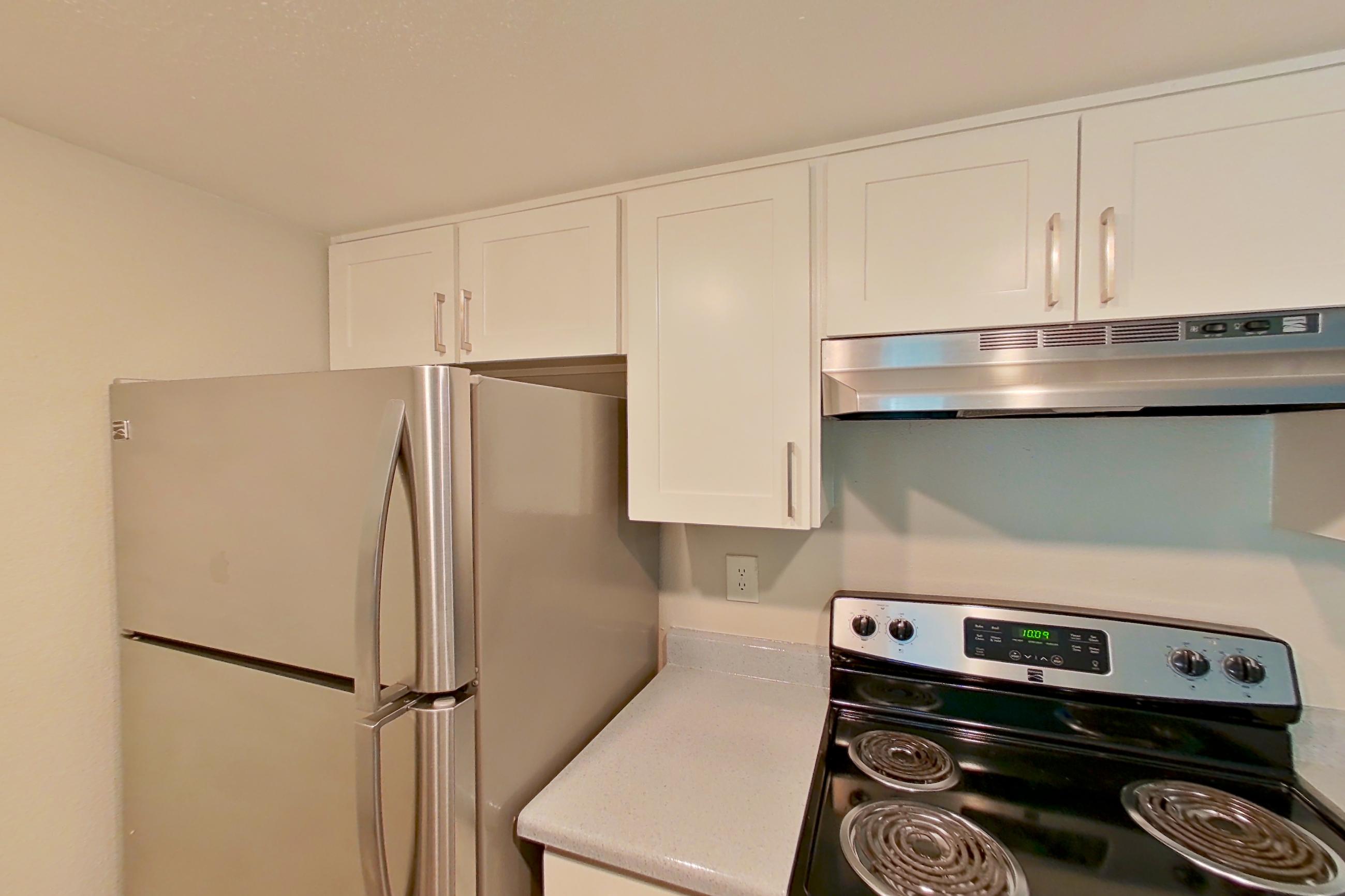 Kitchen with dishwasher, electric range, light countertops, light stone countertops, light wood-finish flooring, oven/range, range hood, refrigerator, and stainless steel appliances, Apartment 06 at Avana Rancho Cucamonga