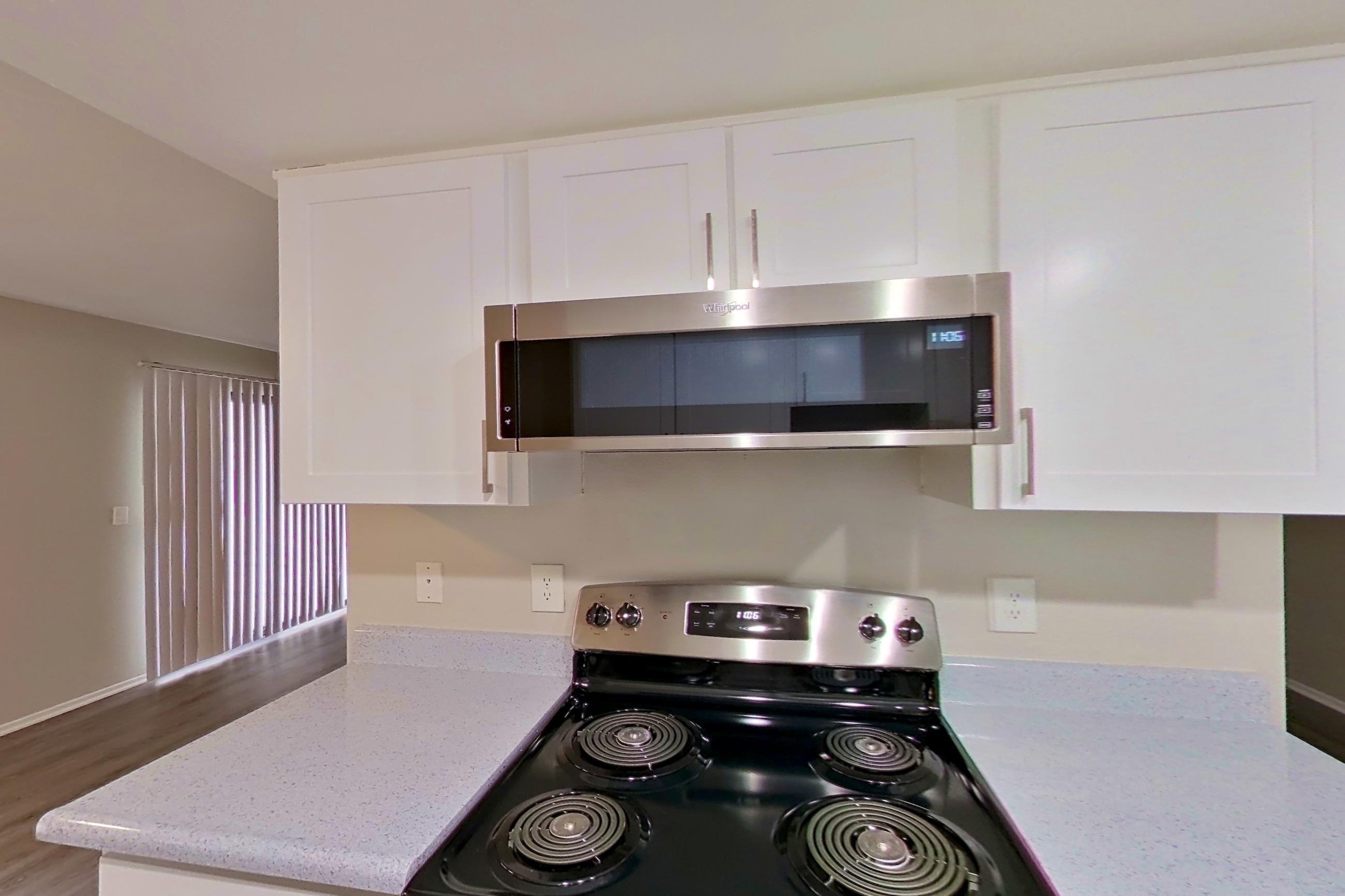 Kitchen with dishwasher, electric range, light countertops, light stone countertops, light wood-finish flooring, microwave, oven/range, refrigerator, and stainless steel appliances, Apartment 12 at Avana Rancho Cucamonga