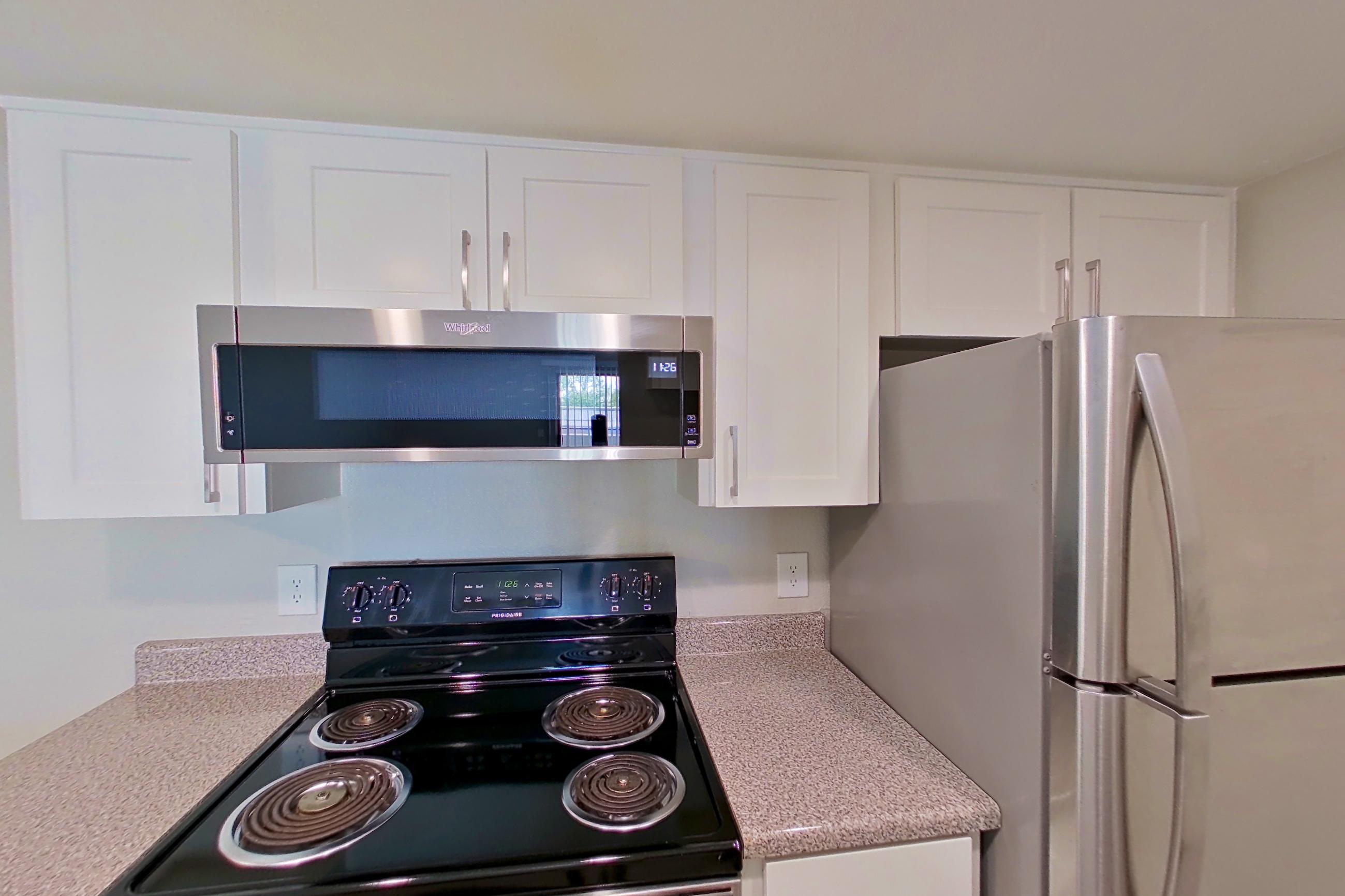 Kitchen with dishwasher, electric range, light countertops, light stone countertops, light wood-finish flooring, oven/range, refrigerator, and stainless steel appliances, Apartment 24 at Avana Rancho Cucamonga