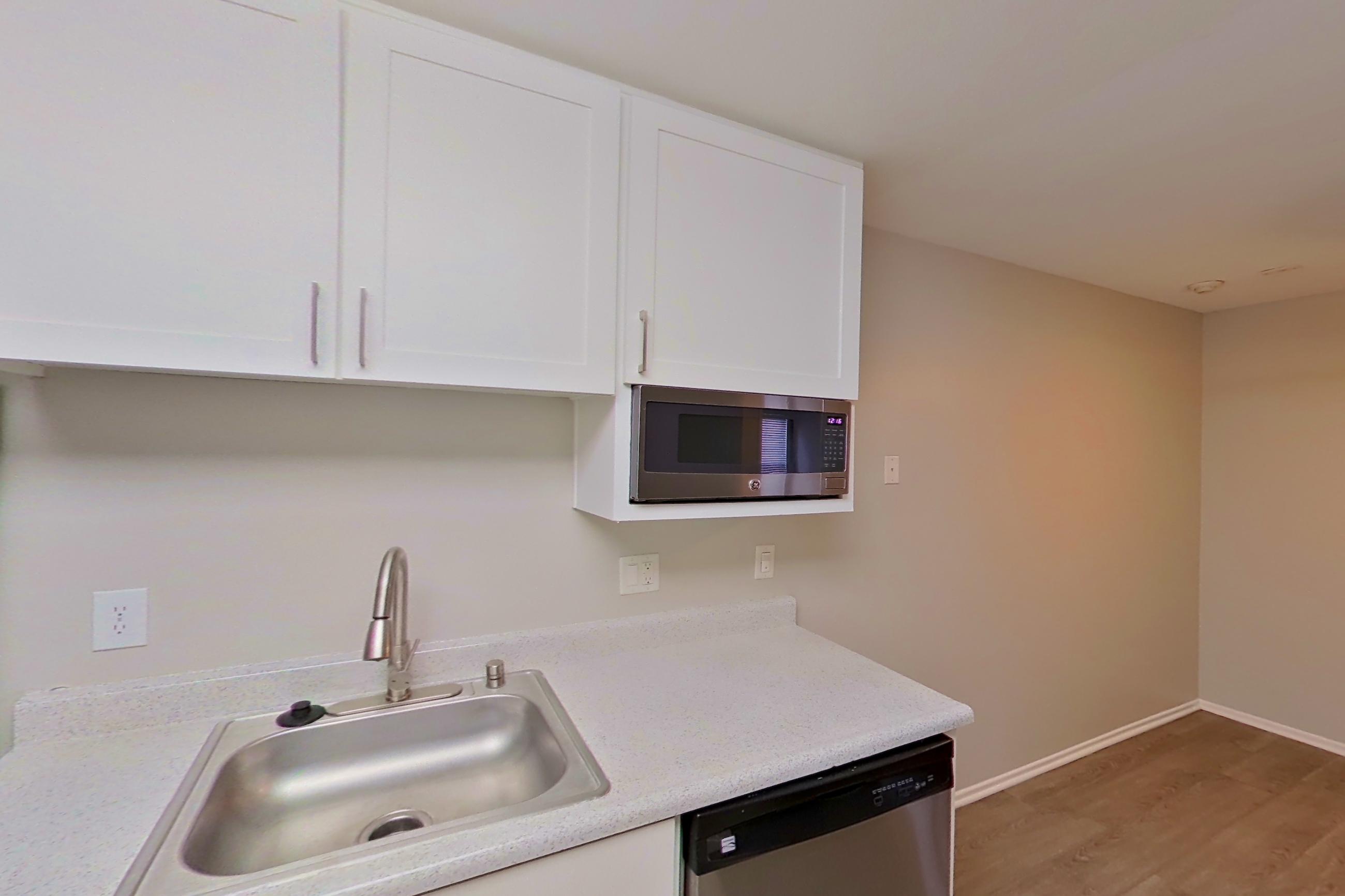 Kitchen with dishwasher, electric range, light countertops, light stone countertops, light wood-finish flooring, oven/range, range hood, refrigerator, and stainless steel appliances, Apartment 16-14 at Avana Rancho Cucamonga