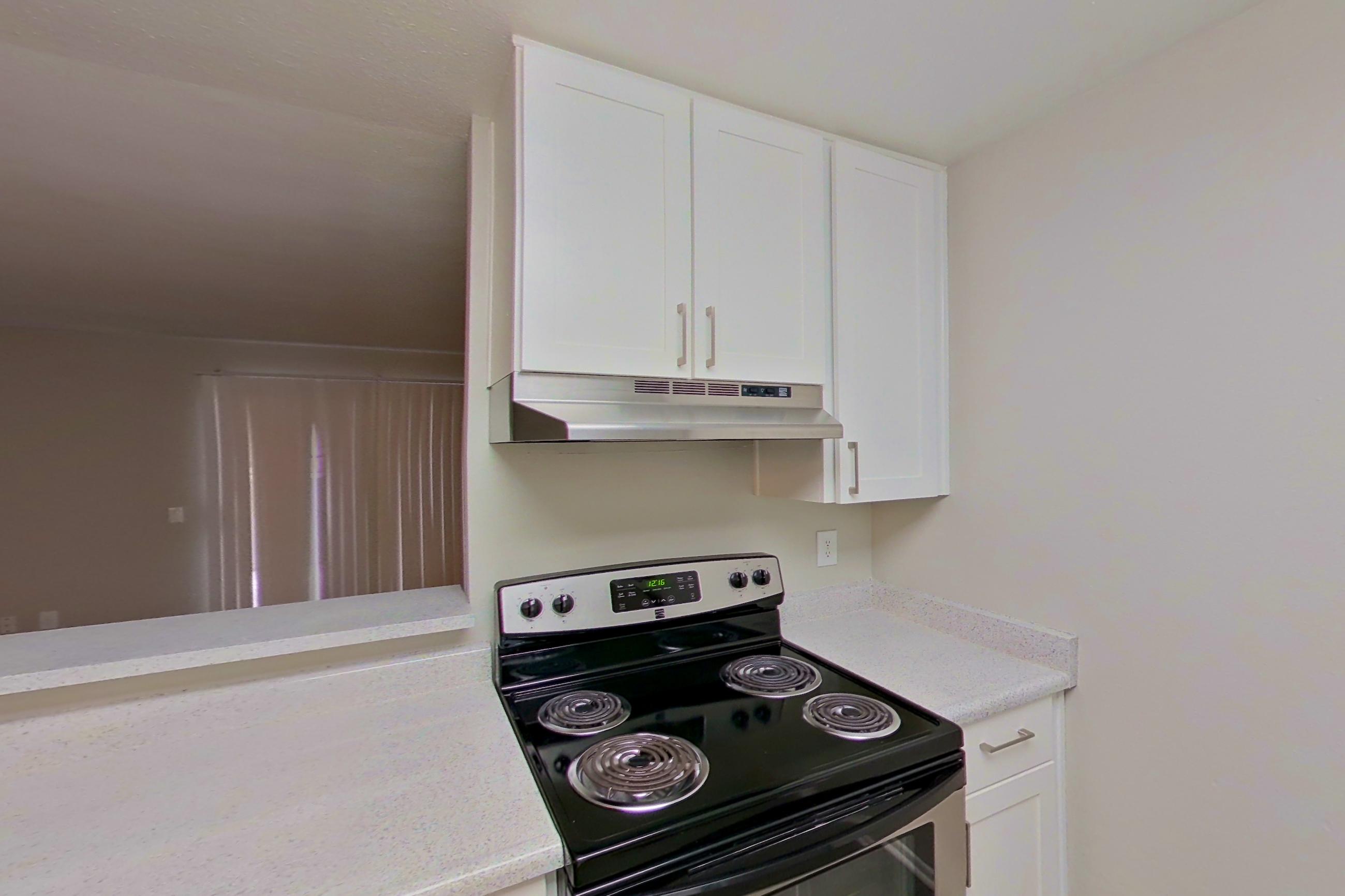 Kitchen with dishwasher, electric range, light countertops, light stone countertops, light wood-finish flooring, oven/range, range hood, refrigerator, and stainless steel appliances, Apartment 16-14 at Avana Rancho Cucamonga