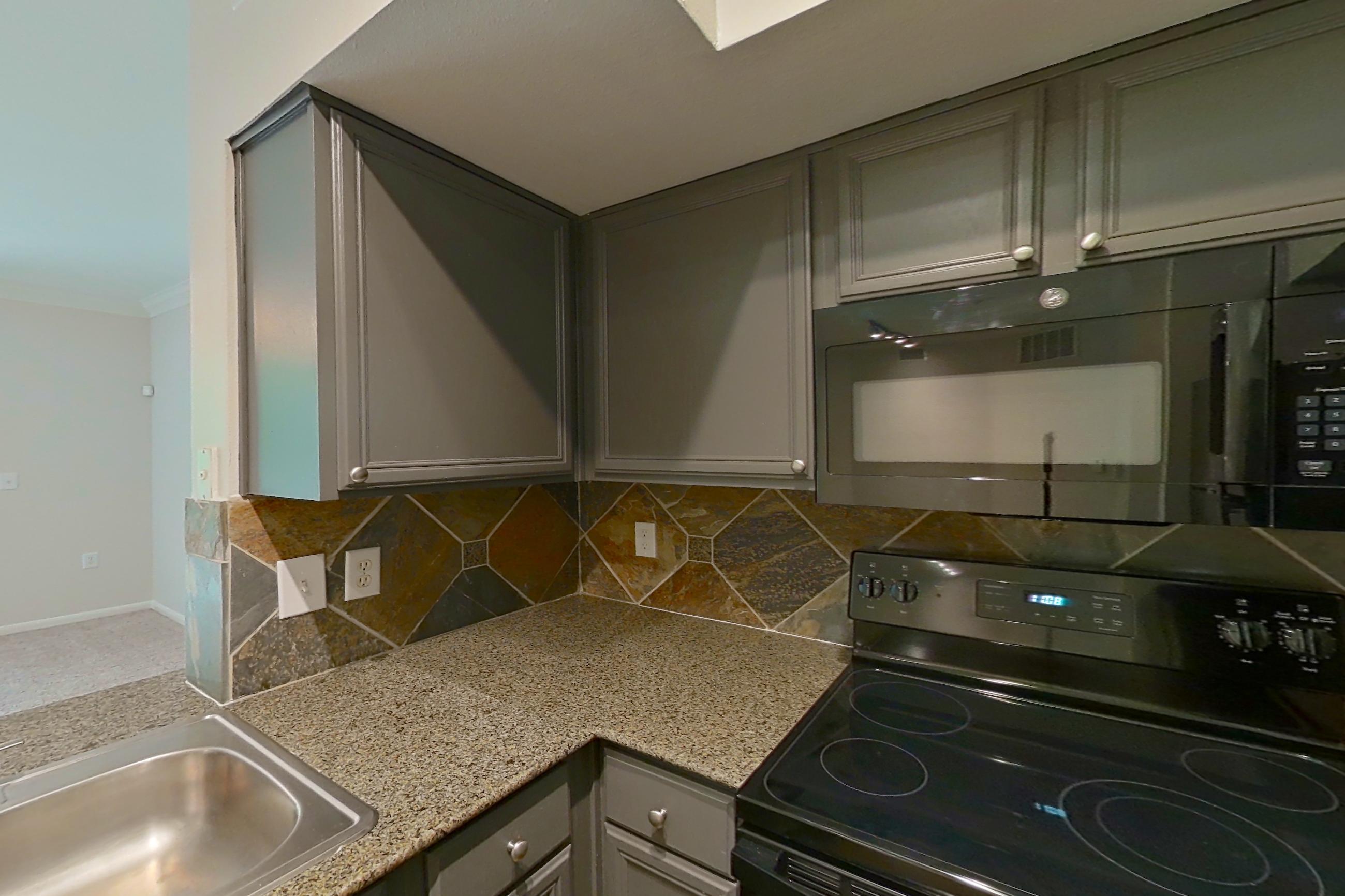 Kitchen with black appliances, dark stone-finish flooring, dishwasher, electric range, light stone countertops, microwave, oven/range, refrigerator, and stainless steel appliances, Apartment 0234 at Portico Kirby