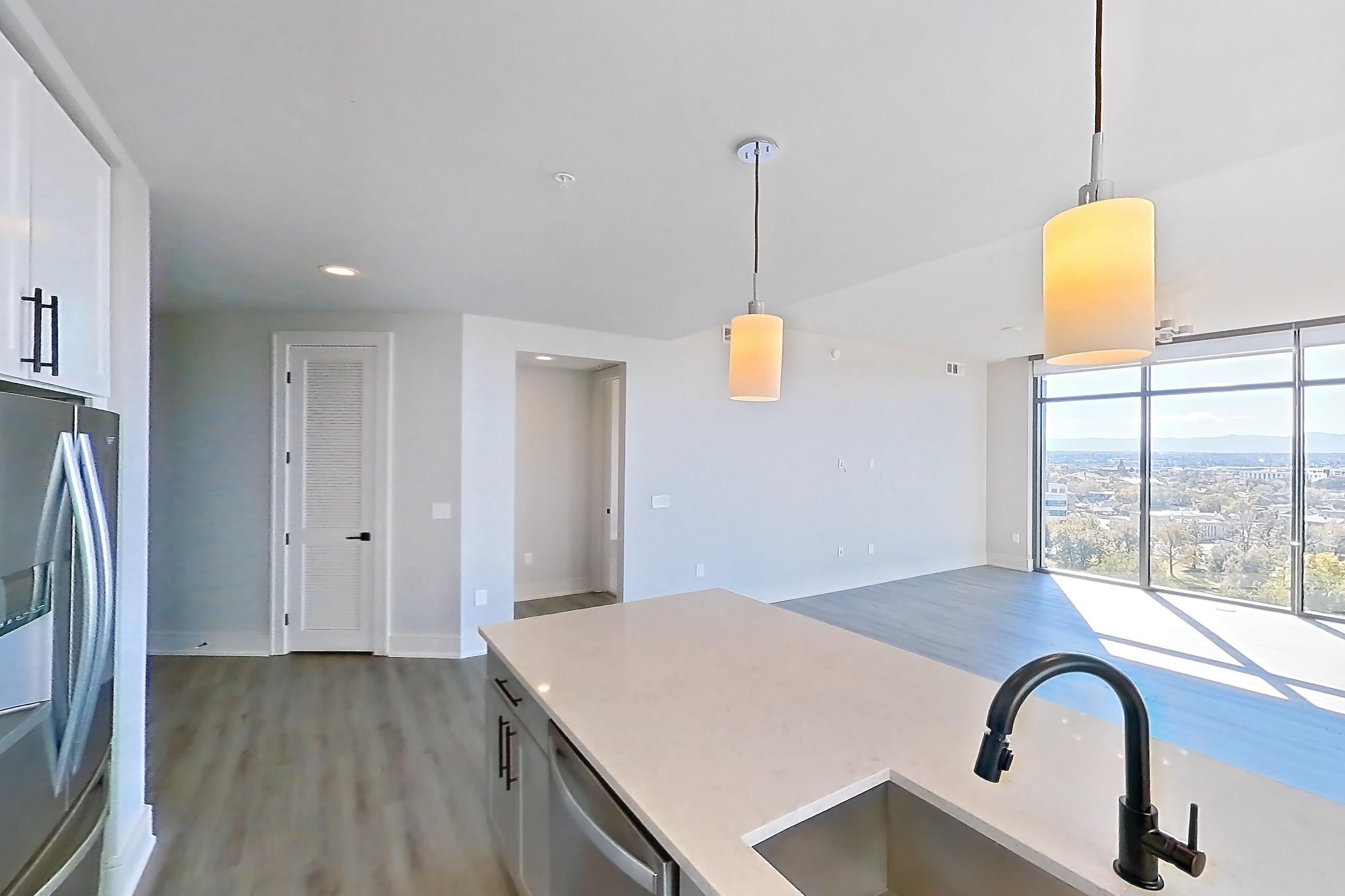 Kitchen with cooktop, dishwasher, double oven, gas cooktop, gas range, light countertops, light stone countertops, light wood-finish flooring, oven/range, refrigerator, stainless steel appliances, and water & ice dispenser, Apartment 1111 at Parq on Speer