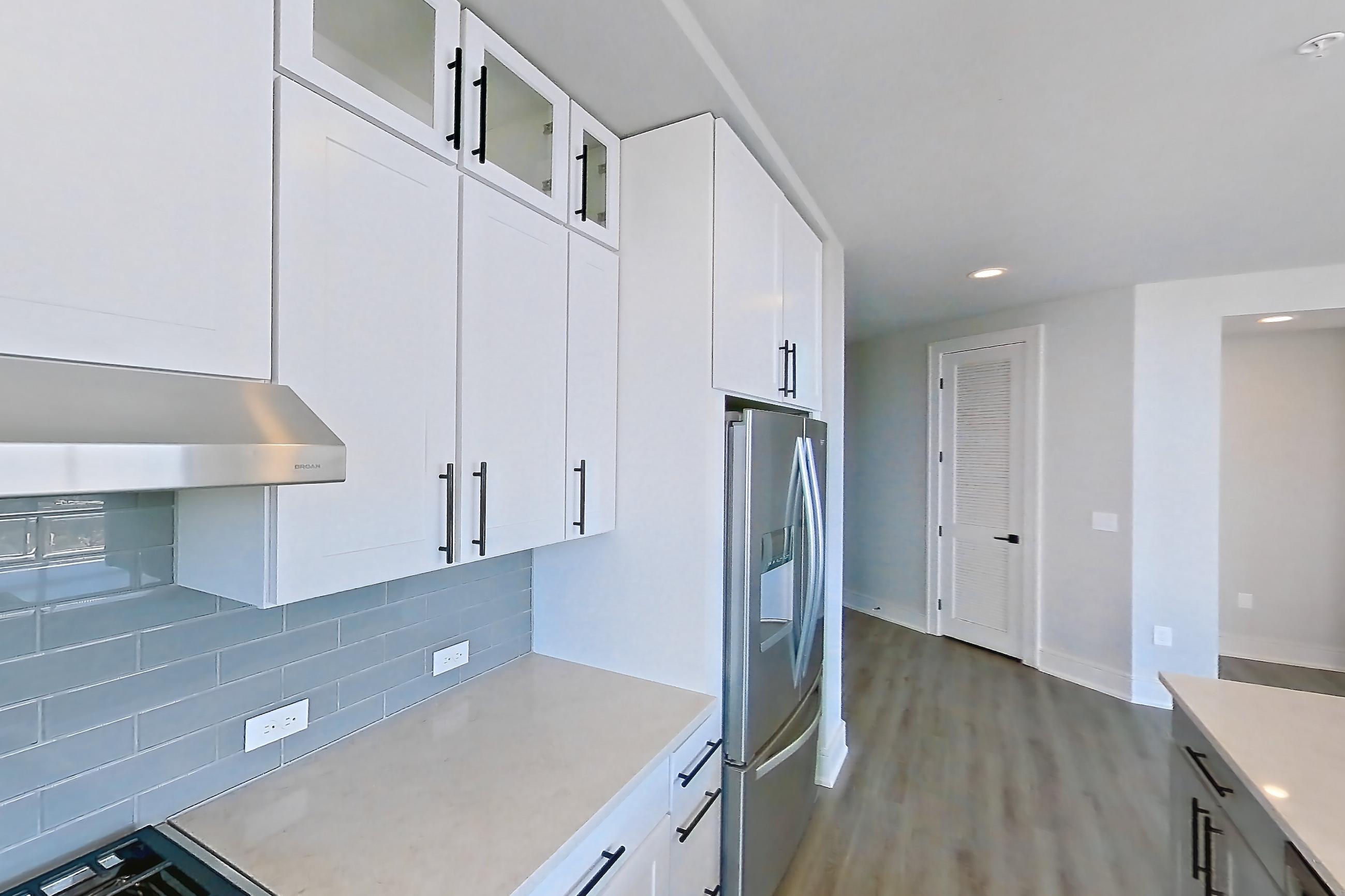 Kitchen with cooktop, dishwasher, double oven, gas cooktop, gas range, light countertops, light stone countertops, light wood-finish flooring, oven/range, refrigerator, stainless steel appliances, and water & ice dispenser, Apartment 1111 at Parq on Speer