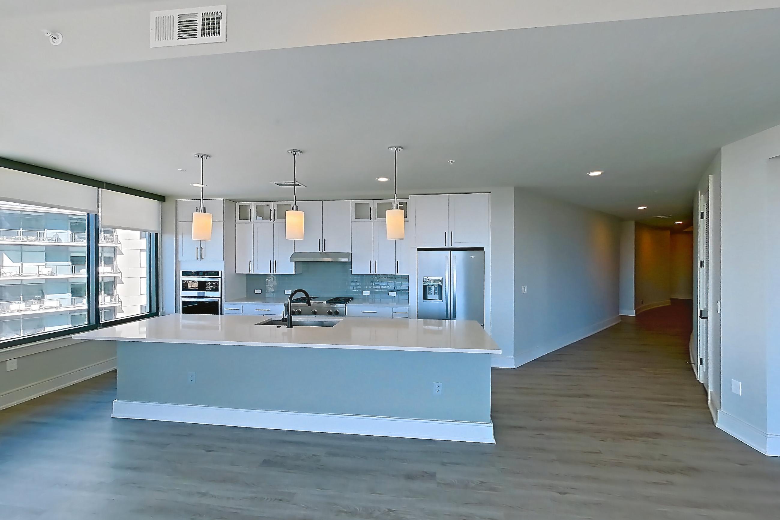 Living space with dark wood-finish flooring, double oven, gas range, kitchen island, light countertops, light stone countertops, oven/range, refrigerator, stainless steel appliances, and water & ice dispenser, Apartment 1111 at Parq on Speer