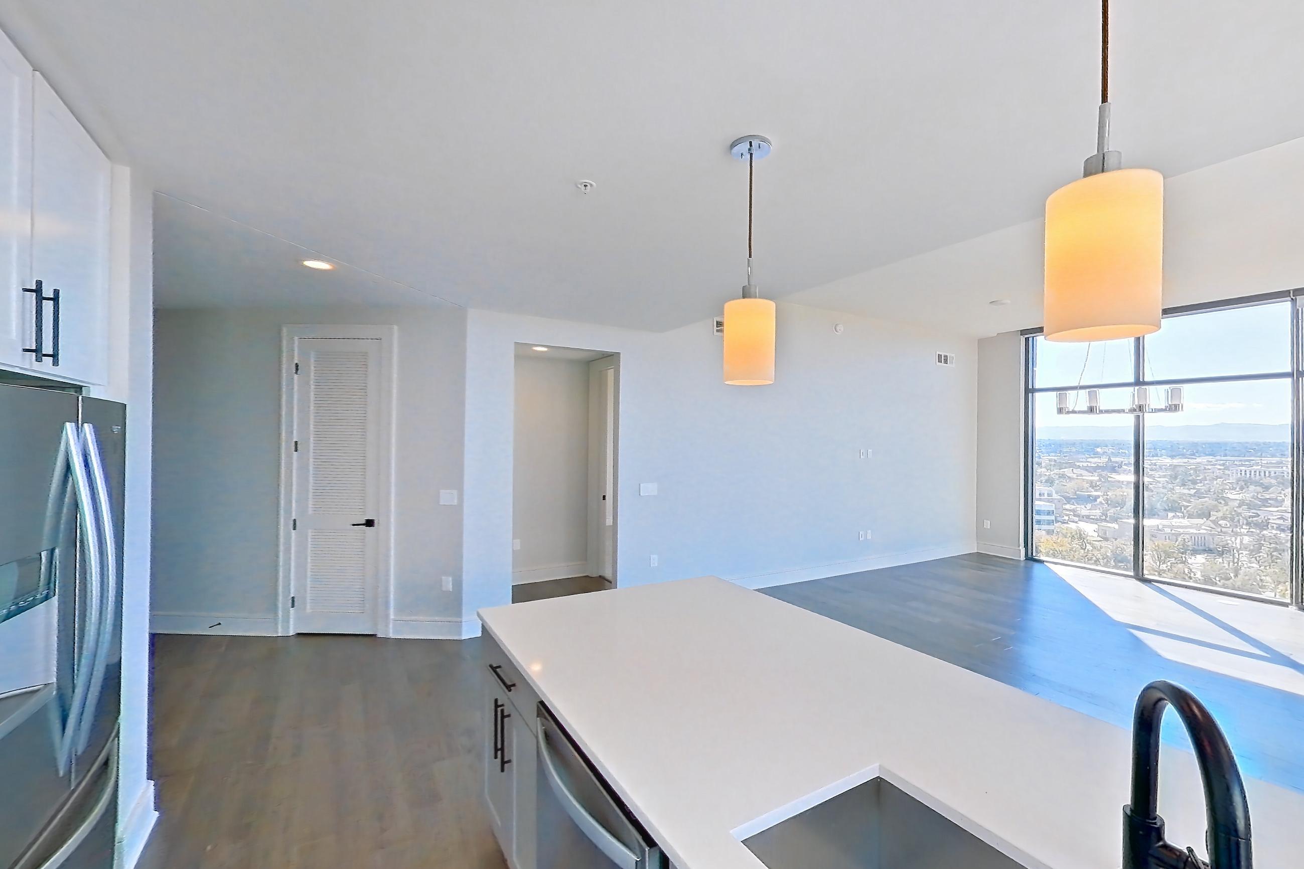 Kitchen with cooktop, dark wood-finish flooring, dishwasher, double oven, gas cooktop, gas range, light countertops, light stone countertops, oven/range, refrigerator, stainless steel appliances, and water & ice dispenser, Apartment 1411 at Parq on Speer
