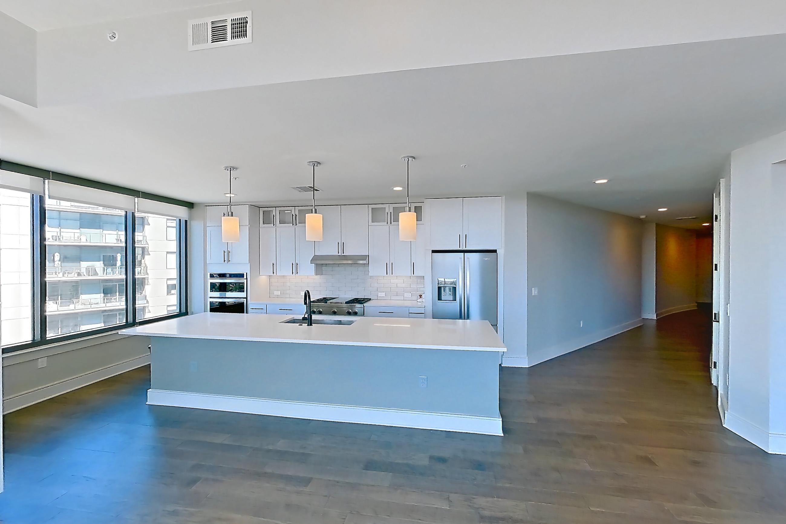 Living space with dark wood-finish flooring, double oven, gas range, kitchen island, light stone countertops, oven/range, refrigerator, stainless steel appliances, and water & ice dispenser, Apartment 1411 at Parq on Speer
