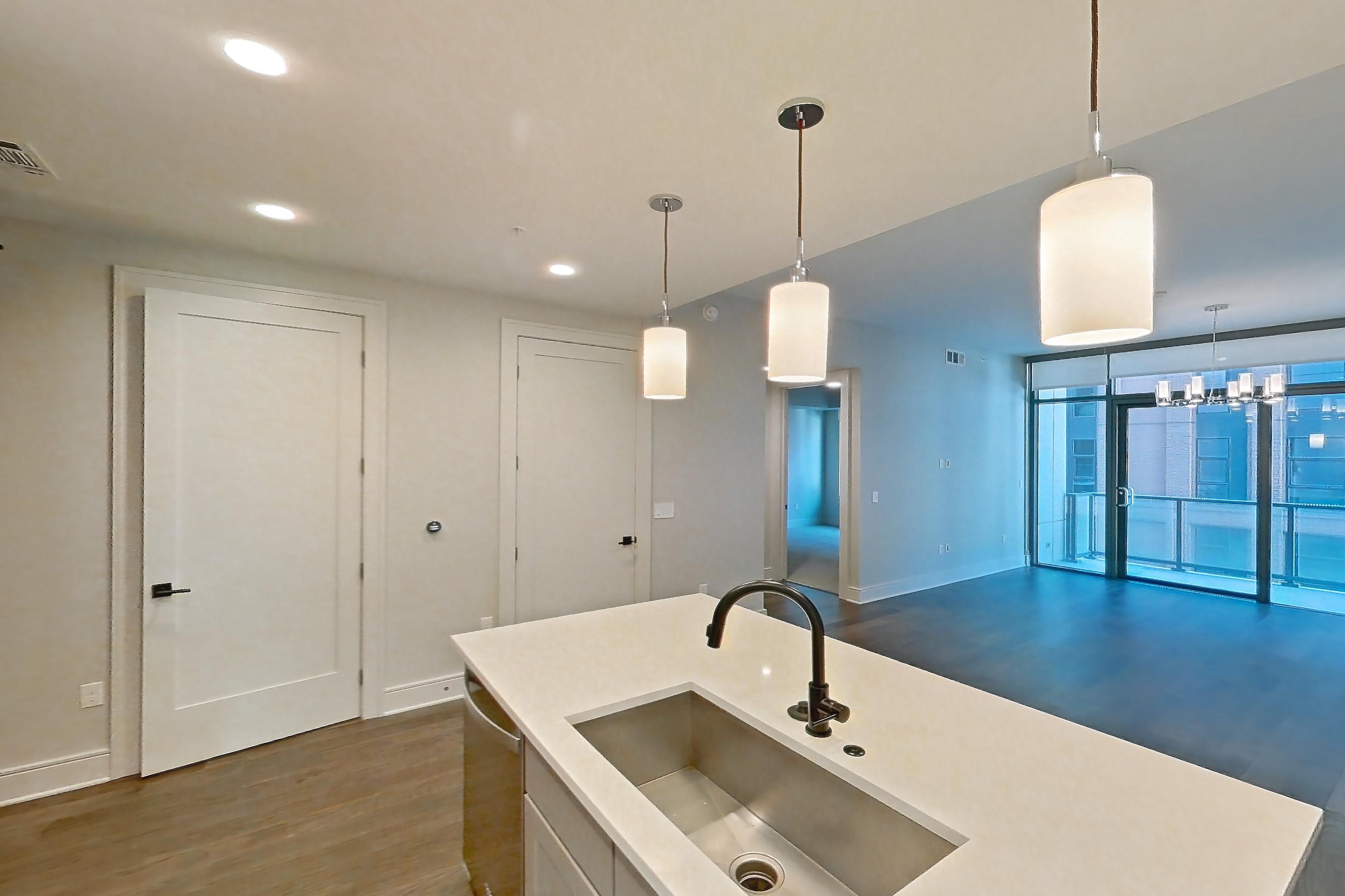 Kitchen with cooktop, dark wood-finish flooring, dishwasher, double oven, gas cooktop, gas range, light countertops, light stone countertops, oven/range, refrigerator, stainless steel appliances, and water & ice dispenser, Apartment 828 at Parq on Speer