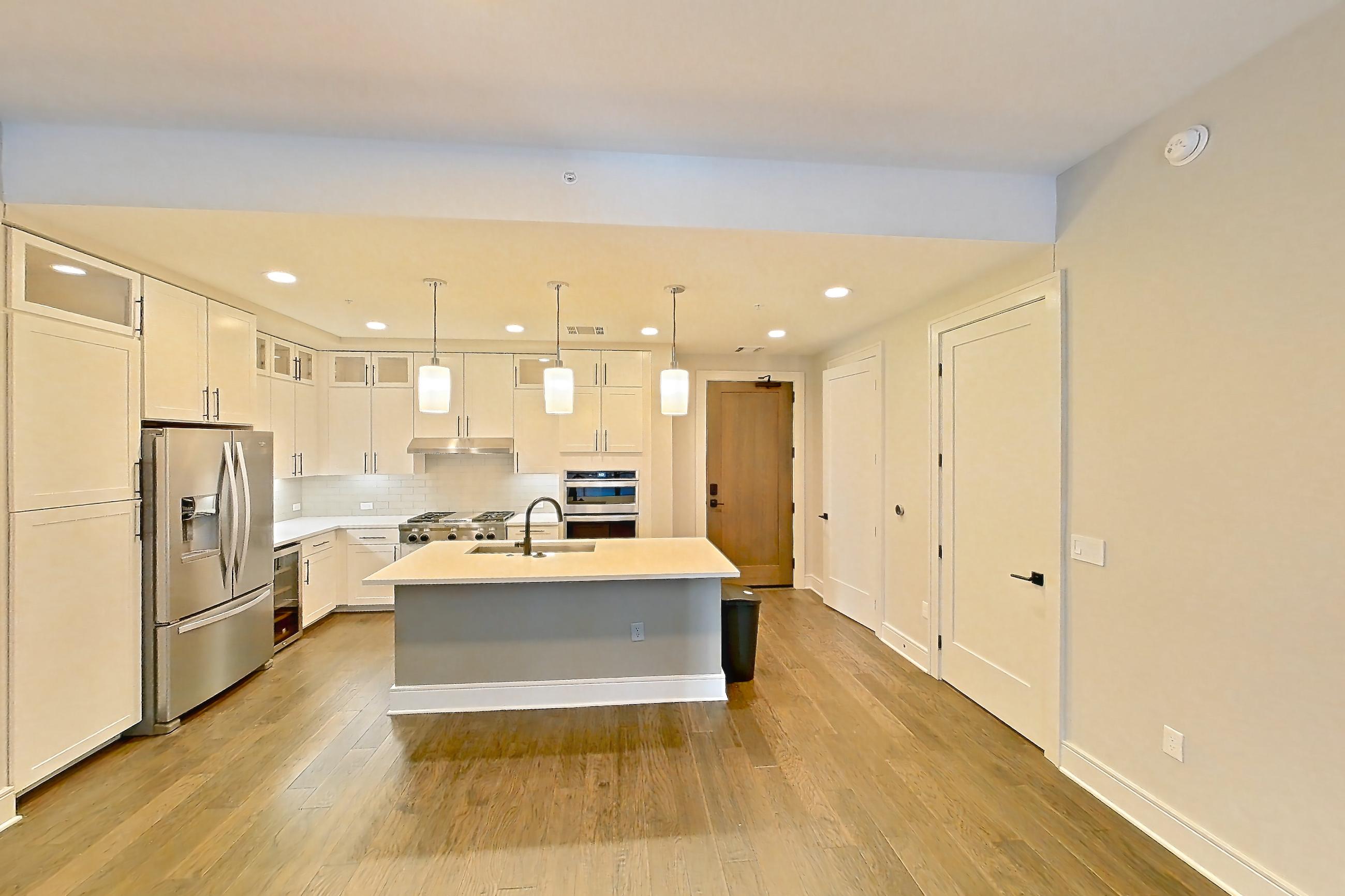 Living space with dark wood-finish flooring, double oven, gas range, kitchen island, light countertops, oven/range, refrigerator, stainless steel appliances, water & ice dispenser, and wood-finish flooring, Apartment 828 at Parq on Speer