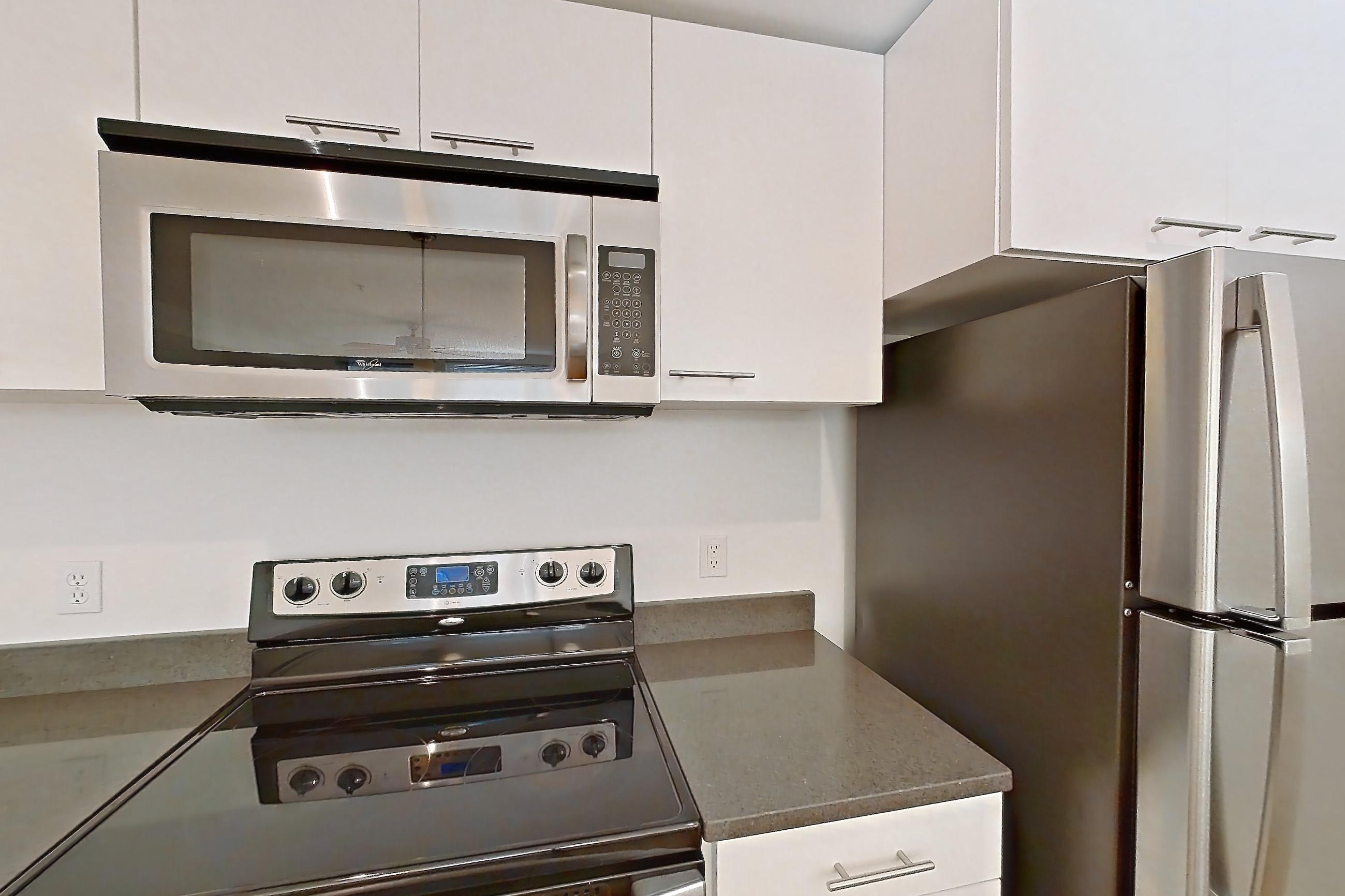 Kitchen with dark countertops, dishwasher, electric range, light countertops, light wood-finish flooring, microwave, oven/range, refrigerator, and stainless steel appliances, Apartment 0255 at Circa Greenlake