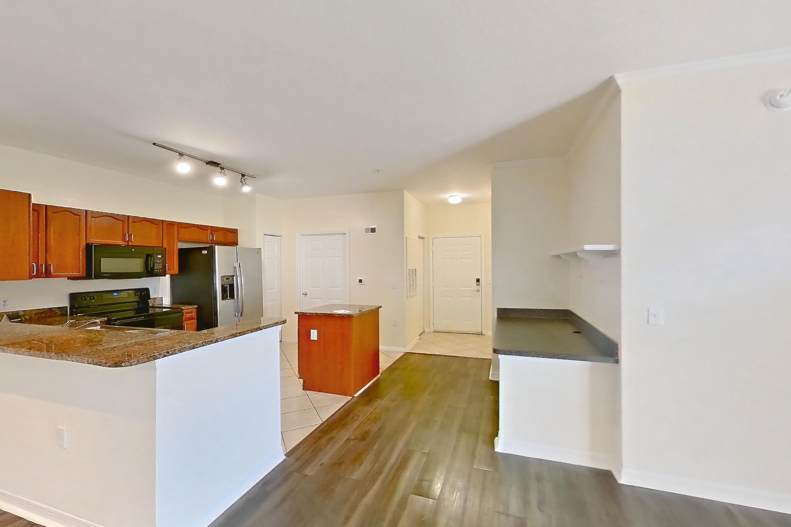 Living room with black appliances, dark stone countertops, dark wood-finish flooring, electric range, light countertops, light wood-finish flooring, oven/range, refrigerator, stainless steel appliances, and water & ice dispenser, Apartment 106 at Tortuga Bay