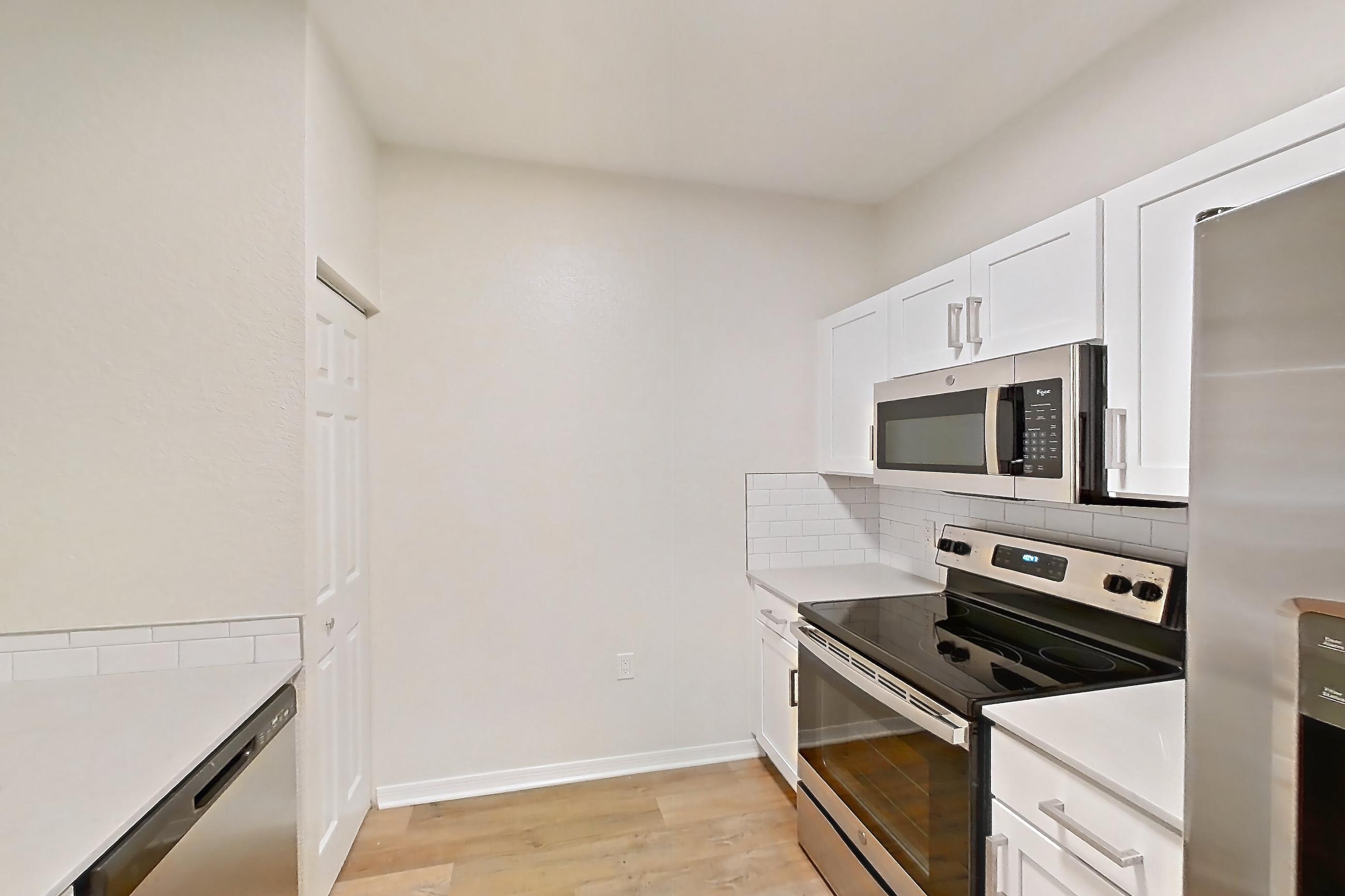 Kitchen with dishwasher, light countertops, light stone countertops, light wood-finish flooring, oven/range, refrigerator, stainless steel appliances, and water & ice dispenser, Apartment 102 at Tortuga Bay