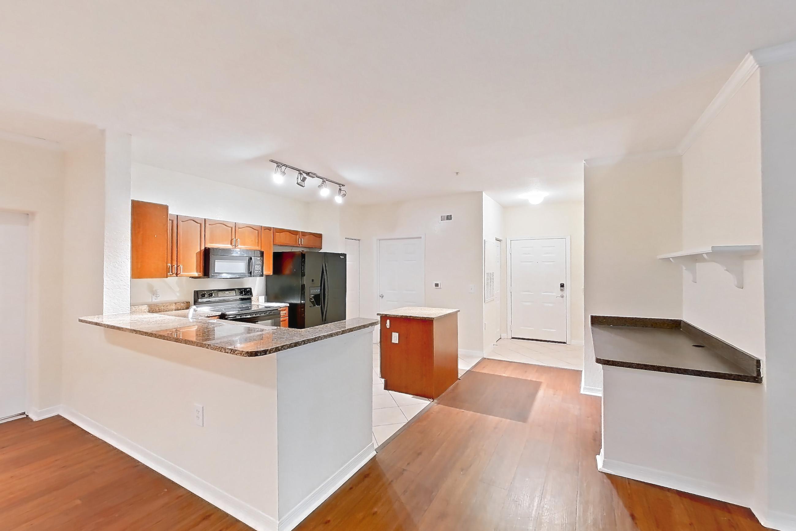 Living room with black appliances, dark stone countertops, dark wood-finish flooring, electric range, light wood-finish flooring, oven/range, refrigerator, water & ice dispenser, and wood-finish flooring, Apartment 106 at Tortuga Bay