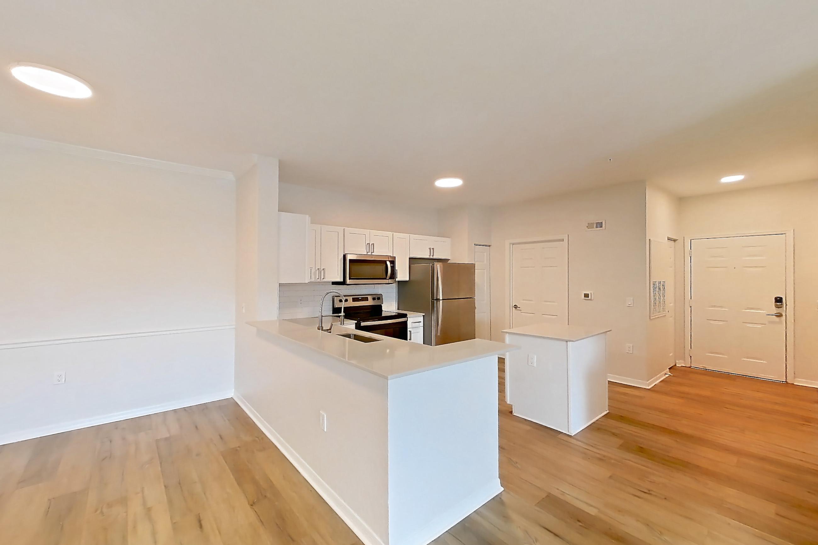 Living room with electric range, light countertops, light wood-finish flooring, oven/range, refrigerator, and stainless steel appliances, Apartment 106 at Tortuga Bay