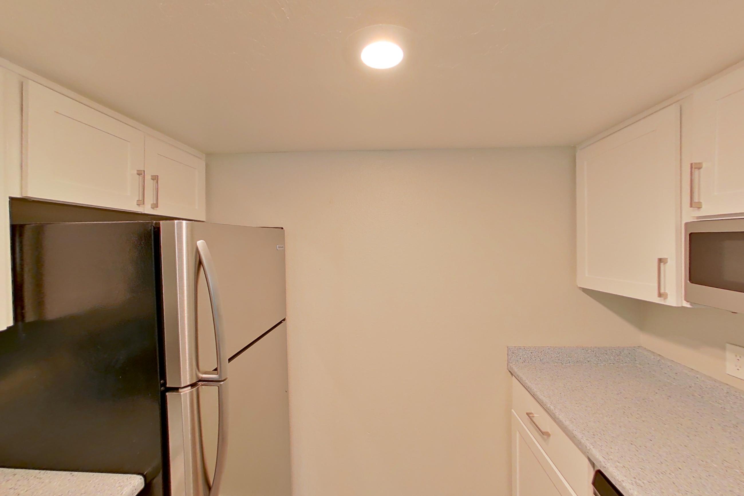 Kitchen with dishwasher, electric range, light stone countertops, light wood-finish flooring, microwave, oven/range, refrigerator, and stainless steel appliances, Apartment 08 at Avana Rancho Cucamonga