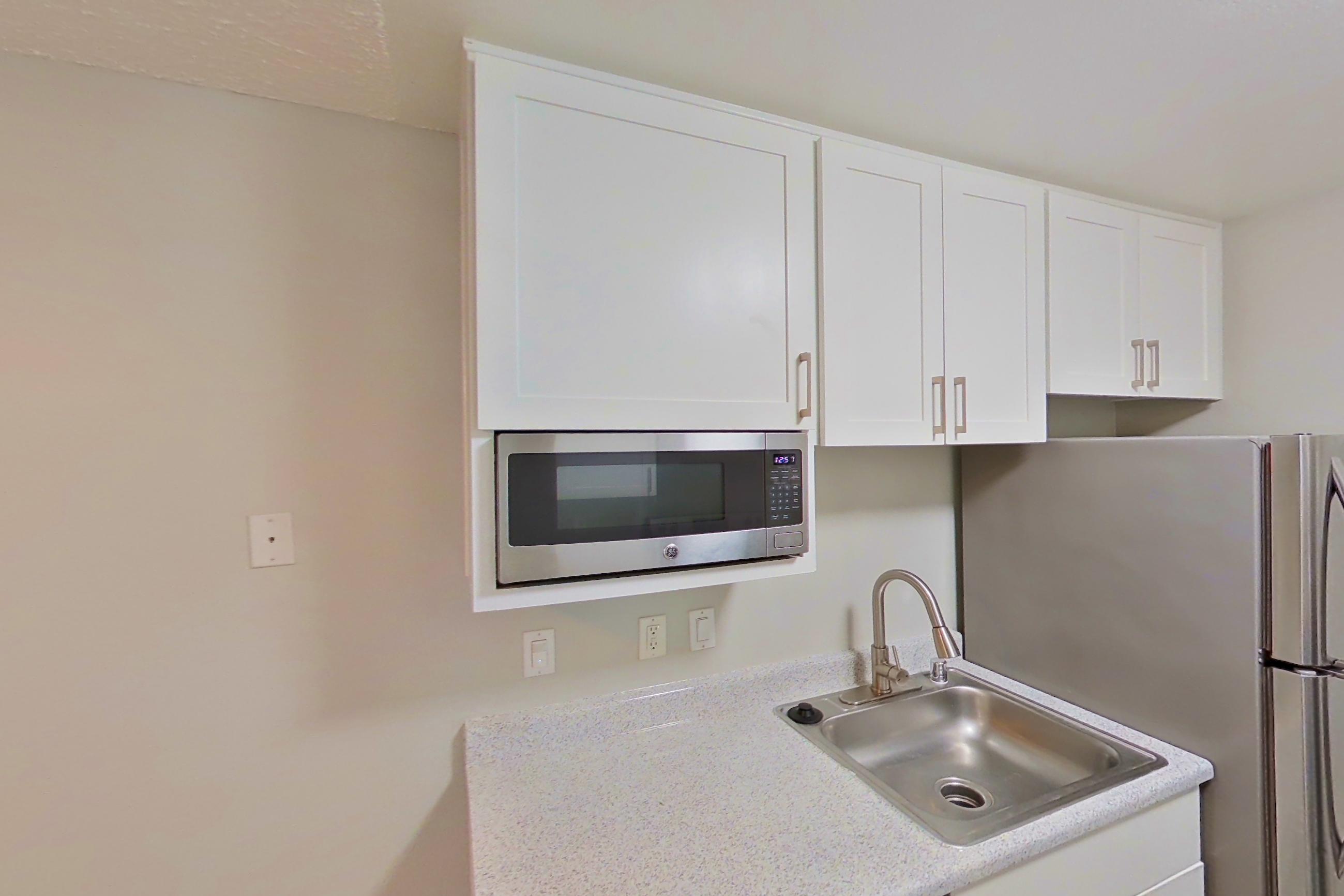 Kitchen with dishwasher, electric range, light countertops, light stone countertops, light wood-finish flooring, microwave, oven/range, and stainless steel appliances, Apartment 17-02 at Avana Rancho Cucamonga