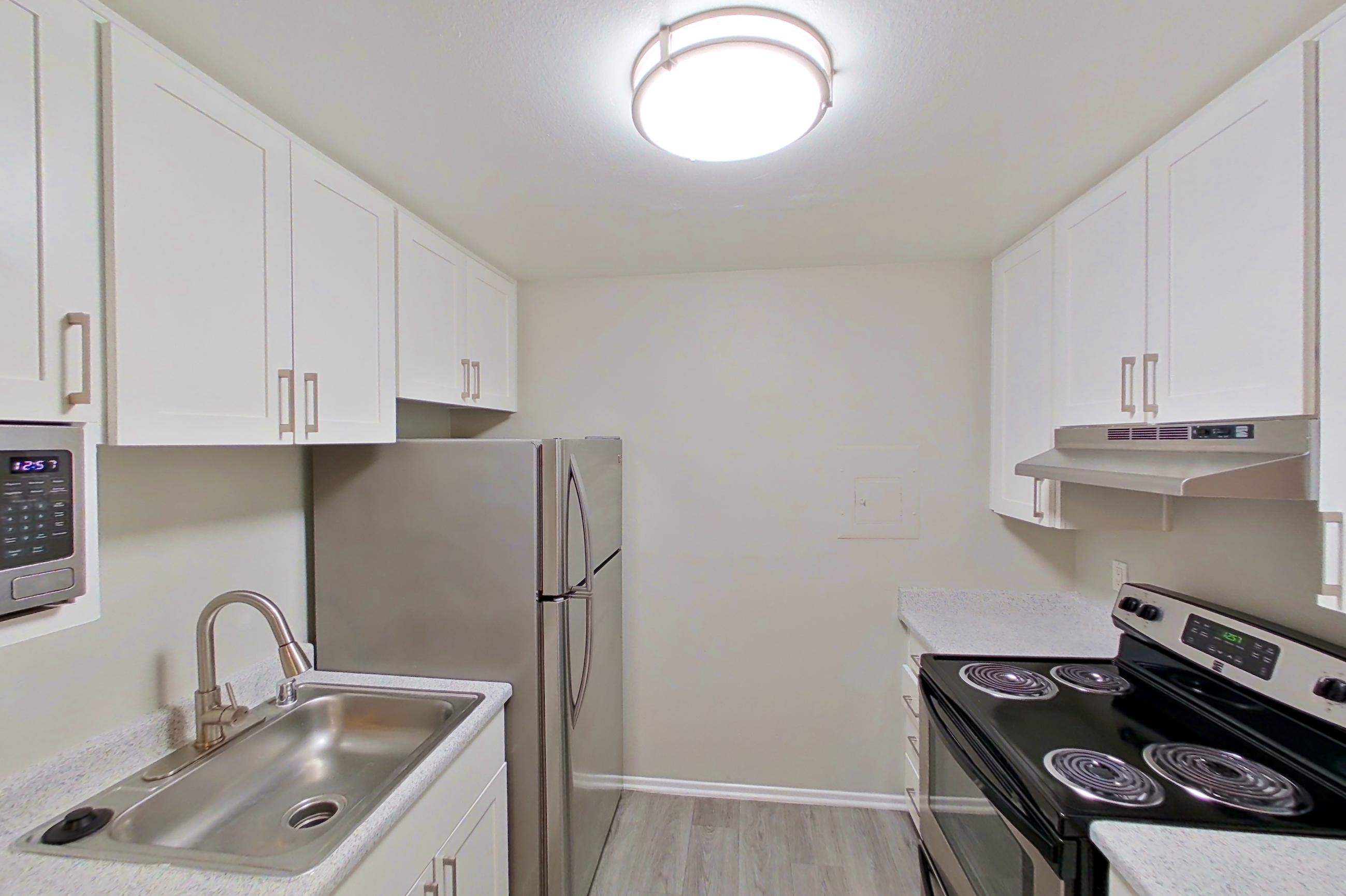 Kitchen with dishwasher, electric range, light countertops, light stone countertops, light wood-finish flooring, microwave, oven/range, and stainless steel appliances, Apartment 17-02 at Avana Rancho Cucamonga