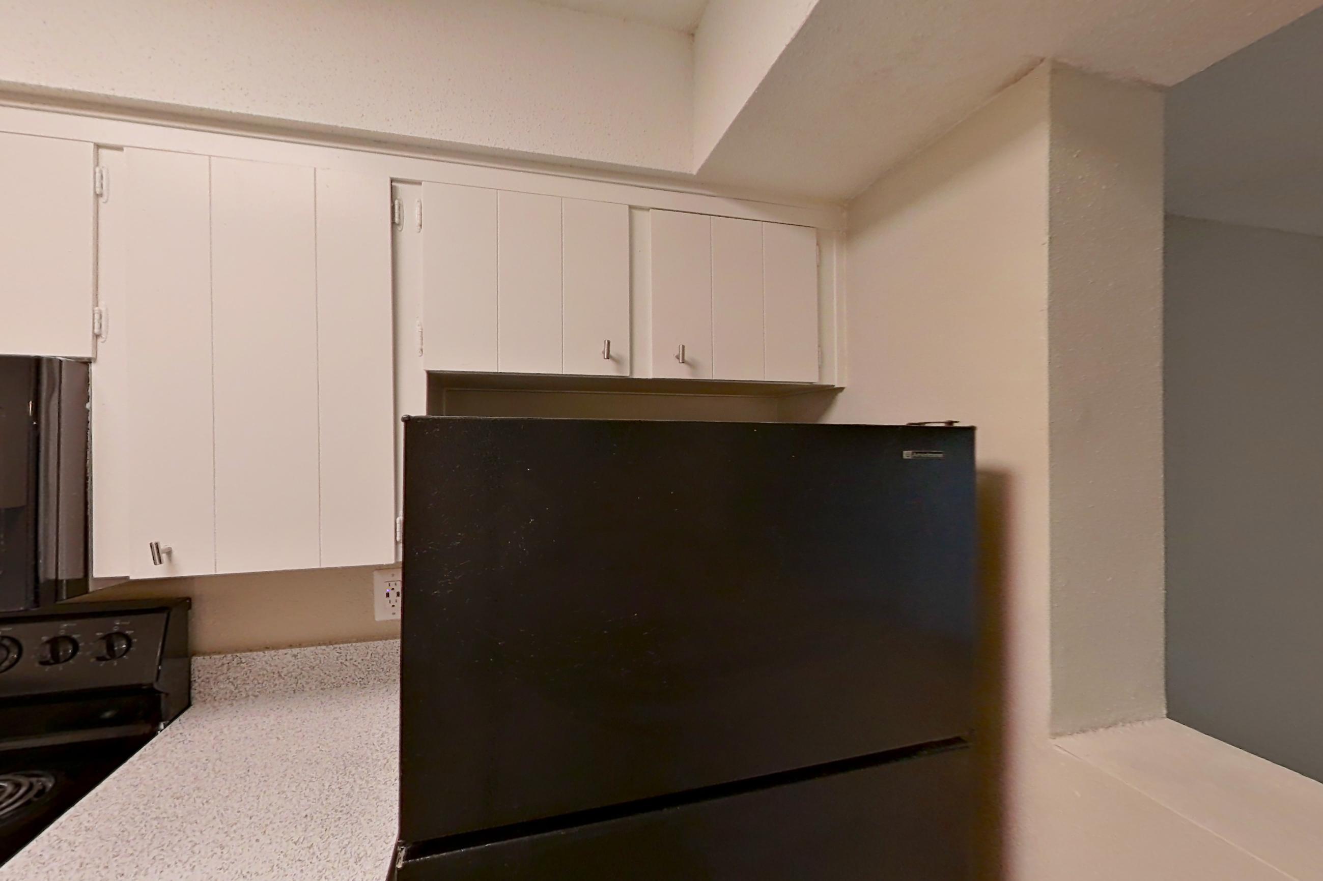 Kitchen with black appliances, dishwasher, electric range, light countertops, light wood-finish flooring, microwave, oven/range, and refrigerator, Apartment 1510C at The Life at Legacy Fountains