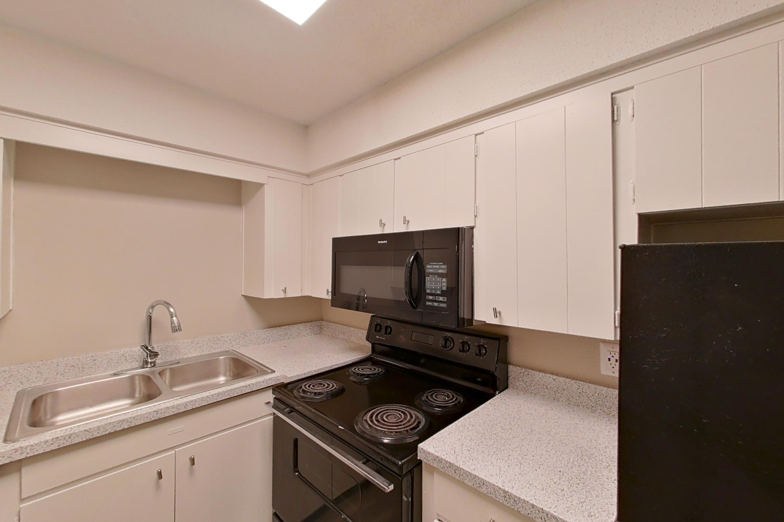 Kitchen with black appliances, dishwasher, electric range, light countertops, light wood-finish flooring, microwave, oven/range, and refrigerator, Apartment 1510C at The Life at Legacy Fountains