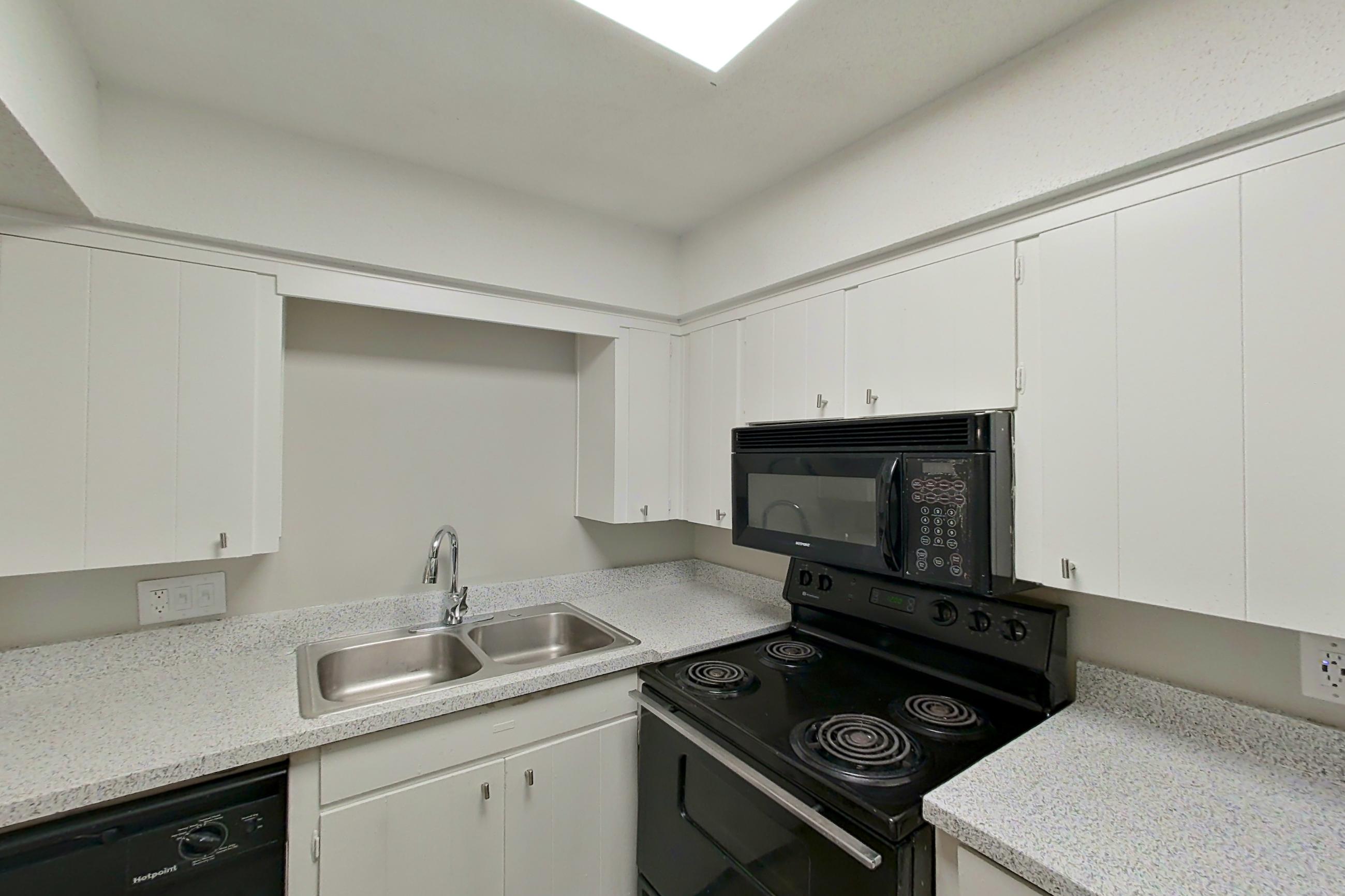 Kitchen with black appliances, dishwasher, electric range, light carpet, light countertops, light stone countertops, light wood-finish flooring, microwave, oven/range, and refrigerator, Apartment 1514C at The Life at Legacy Fountains