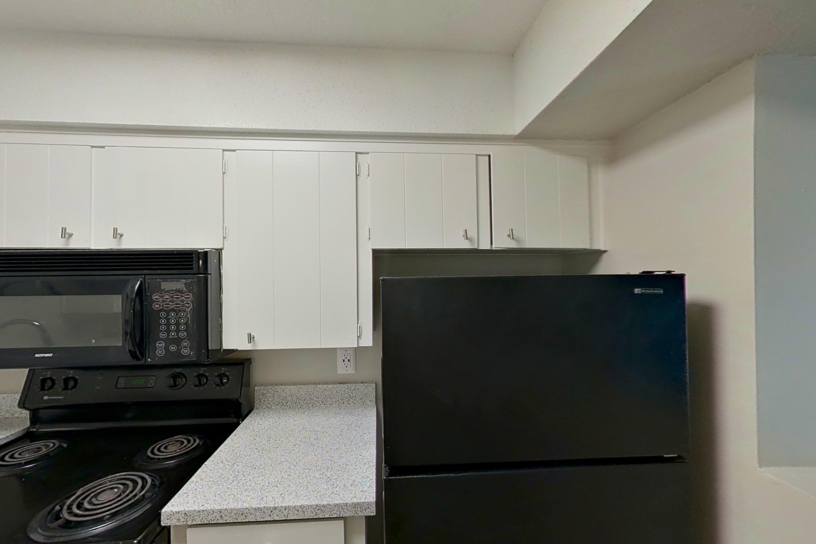 Kitchen with black appliances, dishwasher, electric range, light carpet, light countertops, light stone countertops, light wood-finish flooring, microwave, oven/range, and refrigerator, Apartment 1514C at The Life at Legacy Fountains