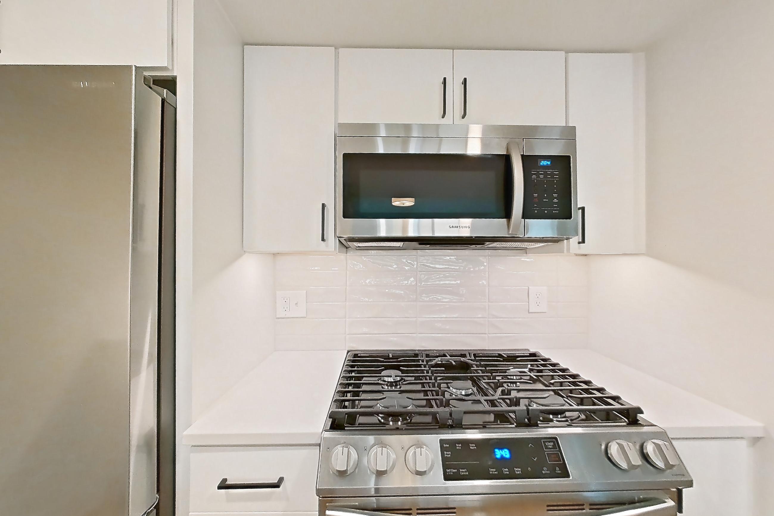 Kitchen with gas range, light countertops, light wood-finish flooring, microwave, oven/range, and stainless steel appliances, Apartment 01-0203 at Cortland Pentagon City