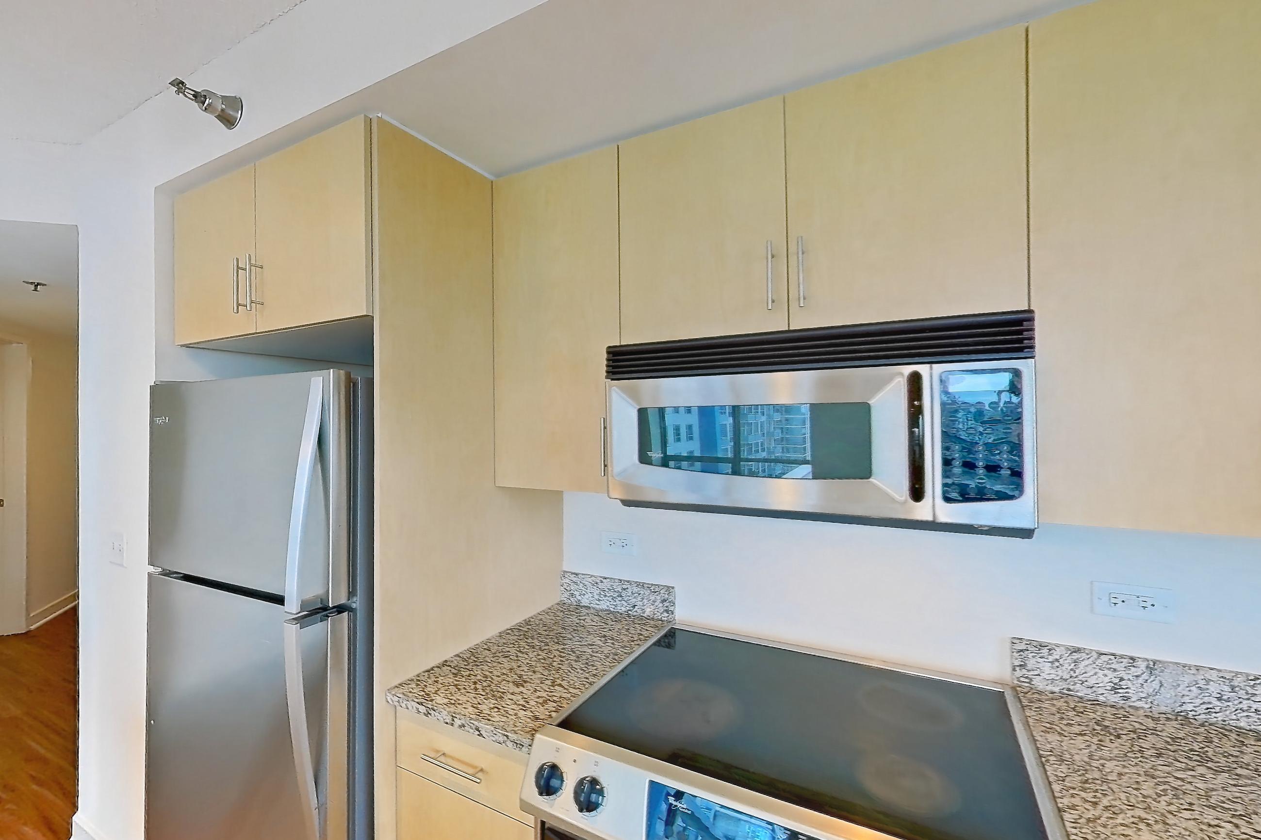 Kitchen with dishwasher, electric range, light countertops, light stone countertops, light wood-finish flooring, microwave, oven/range, refrigerator, and stainless steel appliances, Apartment 00-1909 at Sky55
