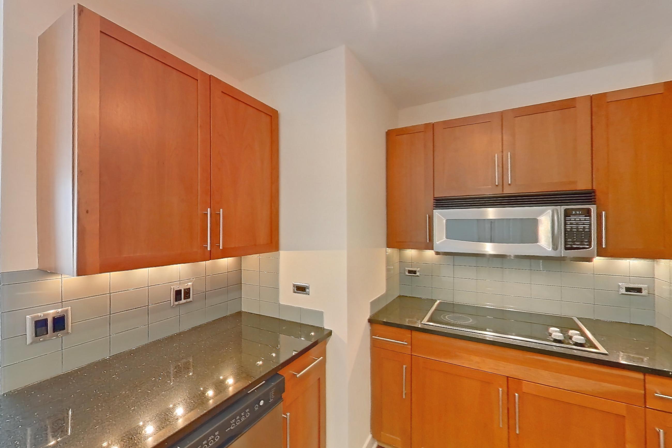 Kitchen with black appliances, cooktop, dark stone countertops, dark wood-finish flooring, dishwasher, double oven, electric cooktop, light countertops, microwave, refrigerator, and stainless steel appliances, Apartment 00-2908 at Sky55
