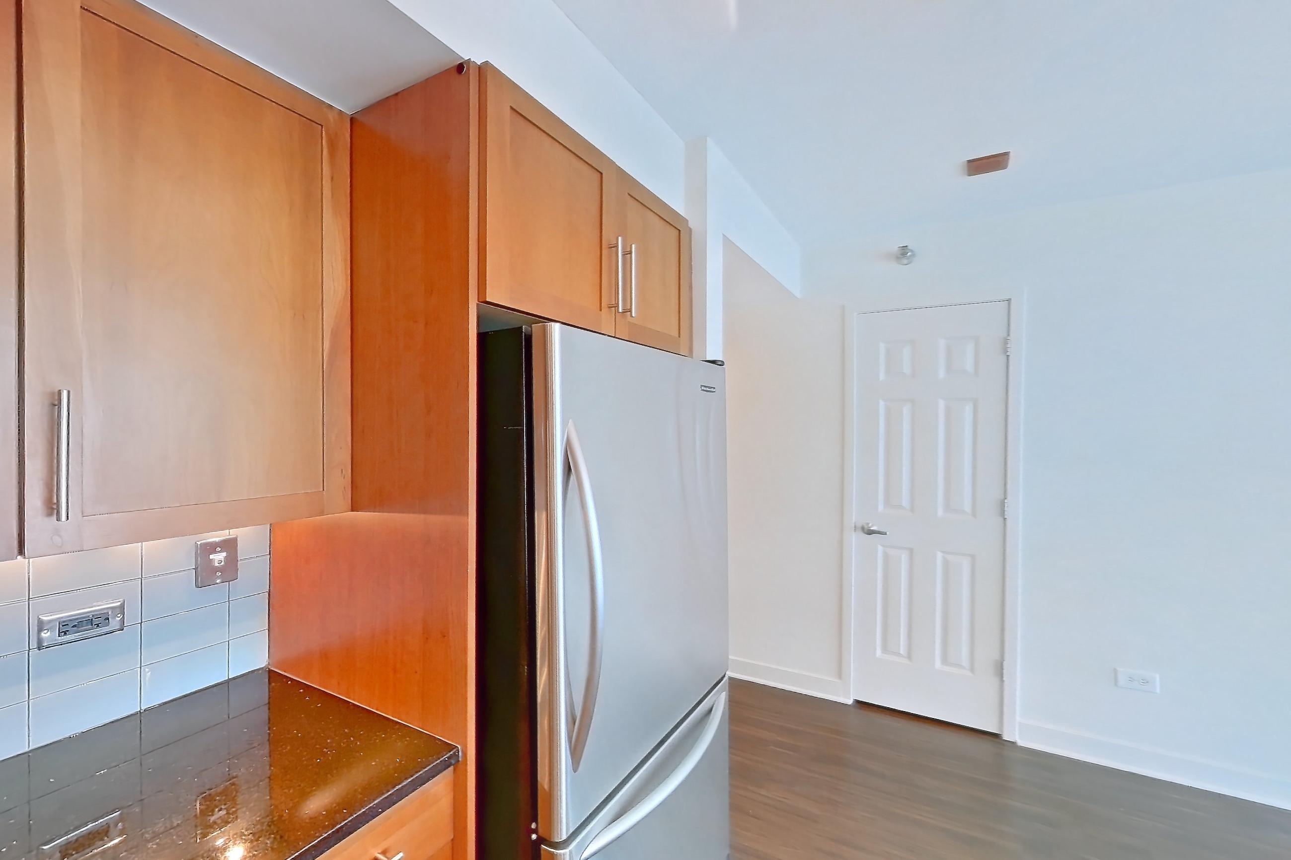 Kitchen with black appliances, cooktop, dark stone countertops, dark wood-finish flooring, dishwasher, double oven, electric cooktop, light countertops, microwave, refrigerator, and stainless steel appliances, Apartment 00-2908 at Sky55