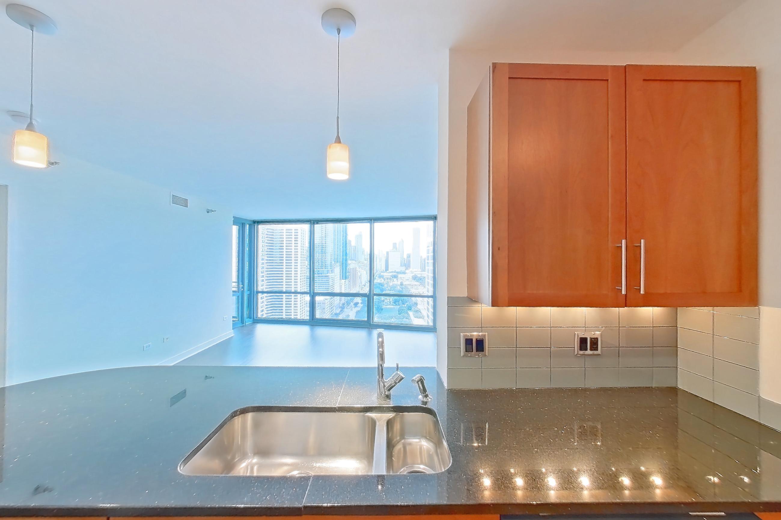 Kitchen with black appliances, cooktop, dark stone countertops, dark wood-finish flooring, dishwasher, double oven, electric cooktop, light countertops, microwave, refrigerator, and stainless steel appliances, Apartment 00-2908 at Sky55