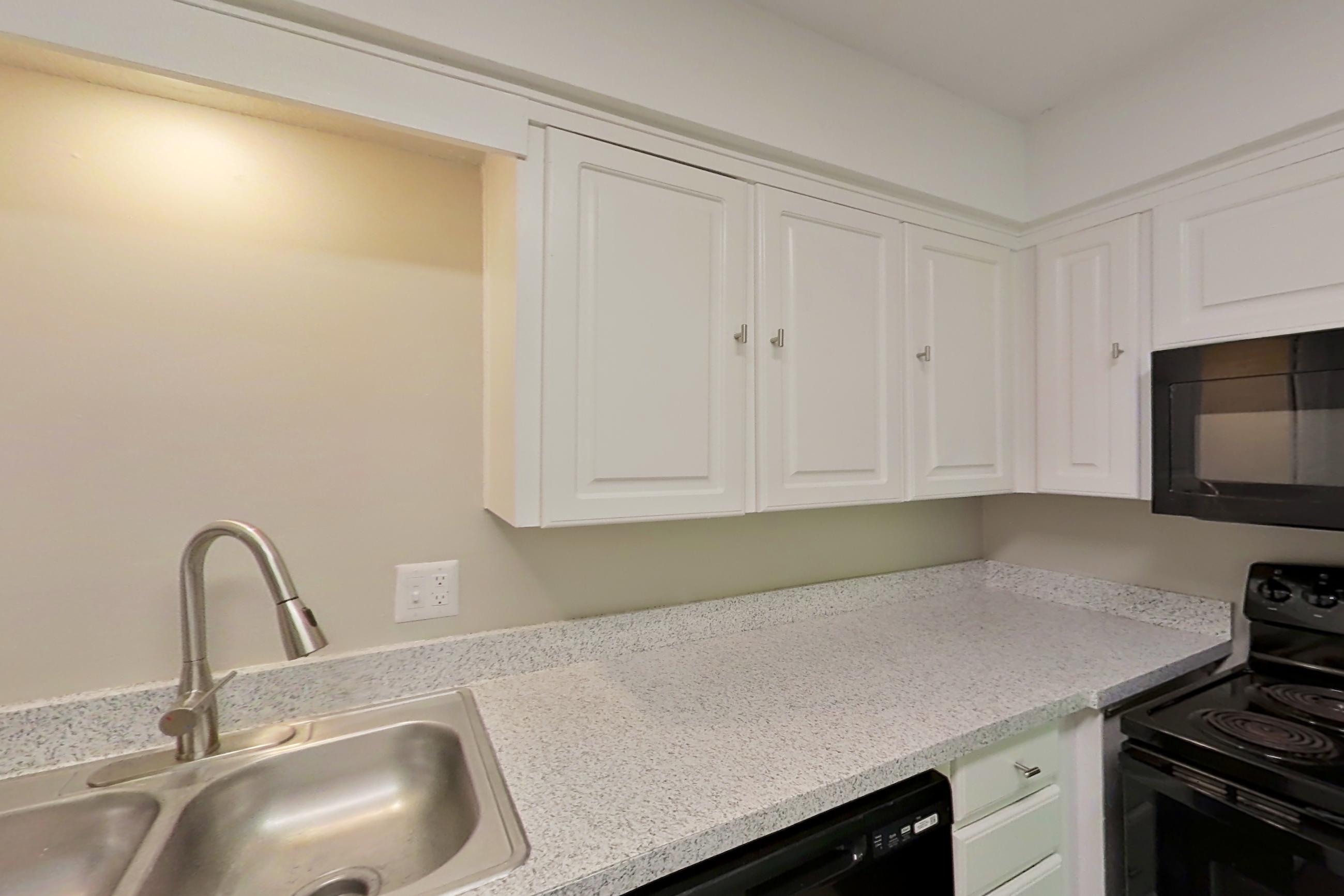 Kitchen with black appliances, dark wood-finish flooring, dishwasher, light countertops, and light stone countertops, Apartment 1415 at The Life at Legacy Fountains