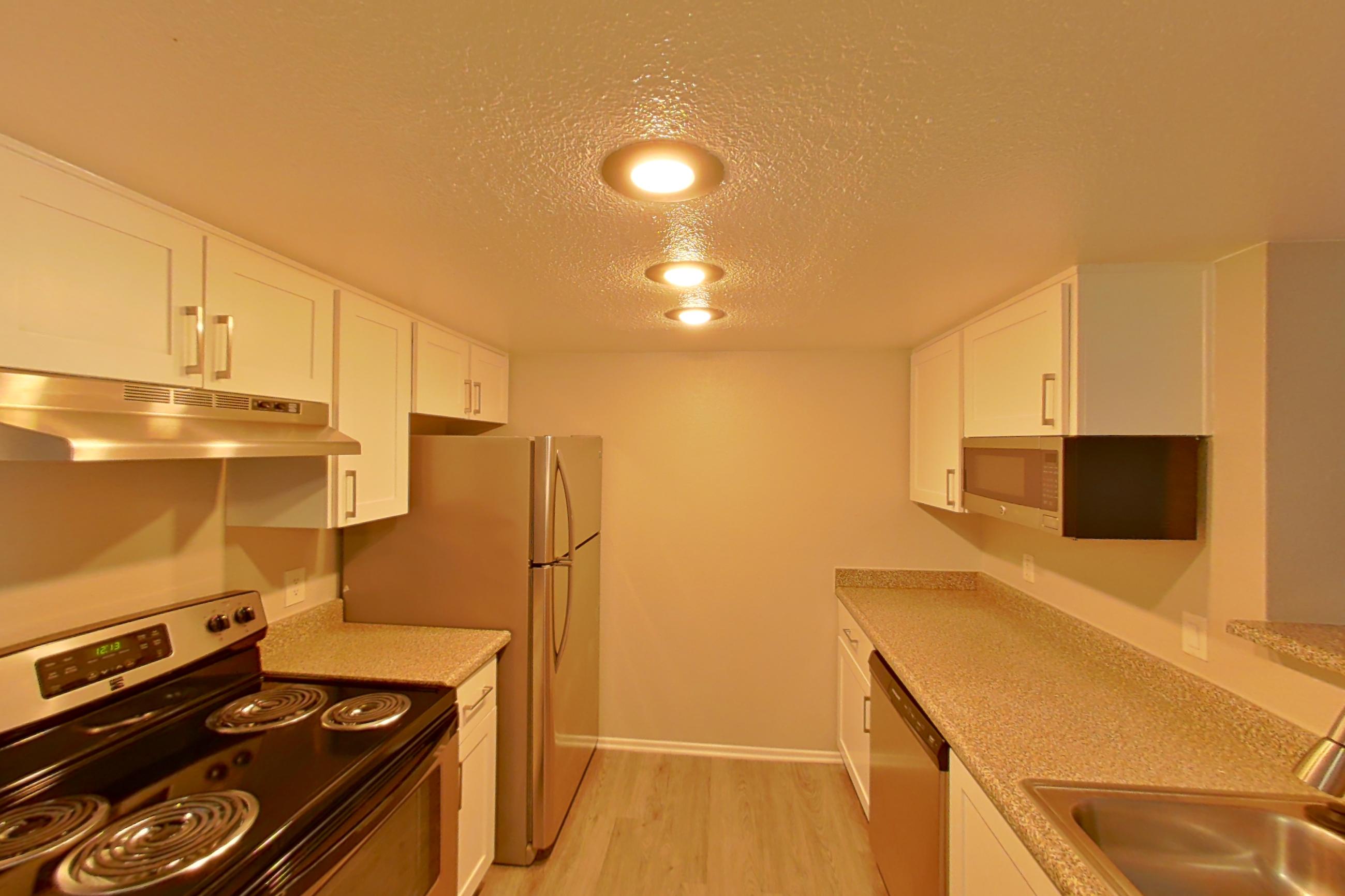 Kitchen with dishwasher, electric range, light countertops, light stone countertops, light wood-finish flooring, oven/range, refrigerator, and stainless steel appliances, Apartment 05 at Avana Rancho Cucamonga
