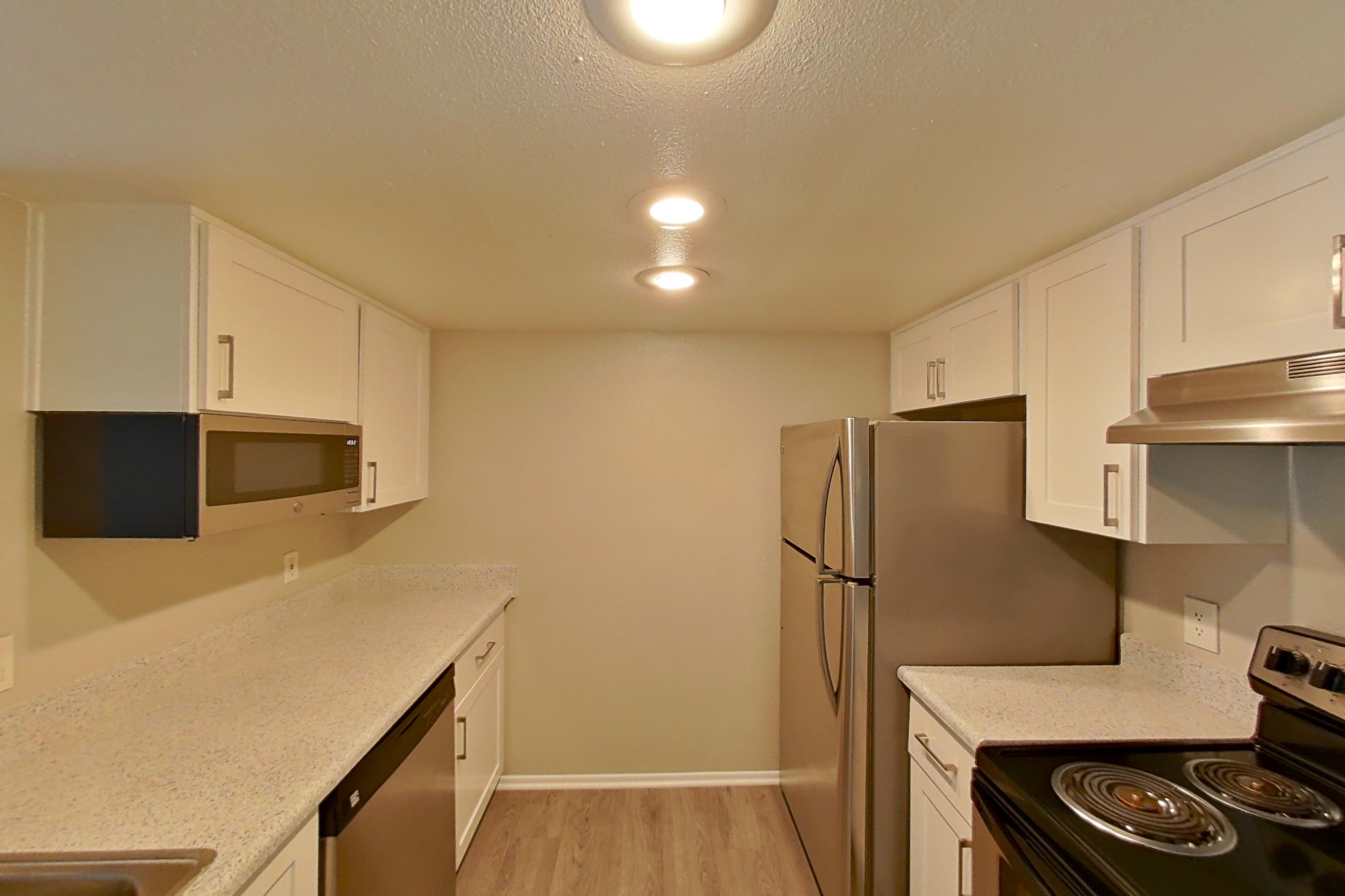Kitchen with dishwasher, electric range, light stone countertops, light wood-finish flooring, microwave, oven/range, stainless steel appliances, and white appliances, Apartment 11 at Avana Rancho Cucamonga