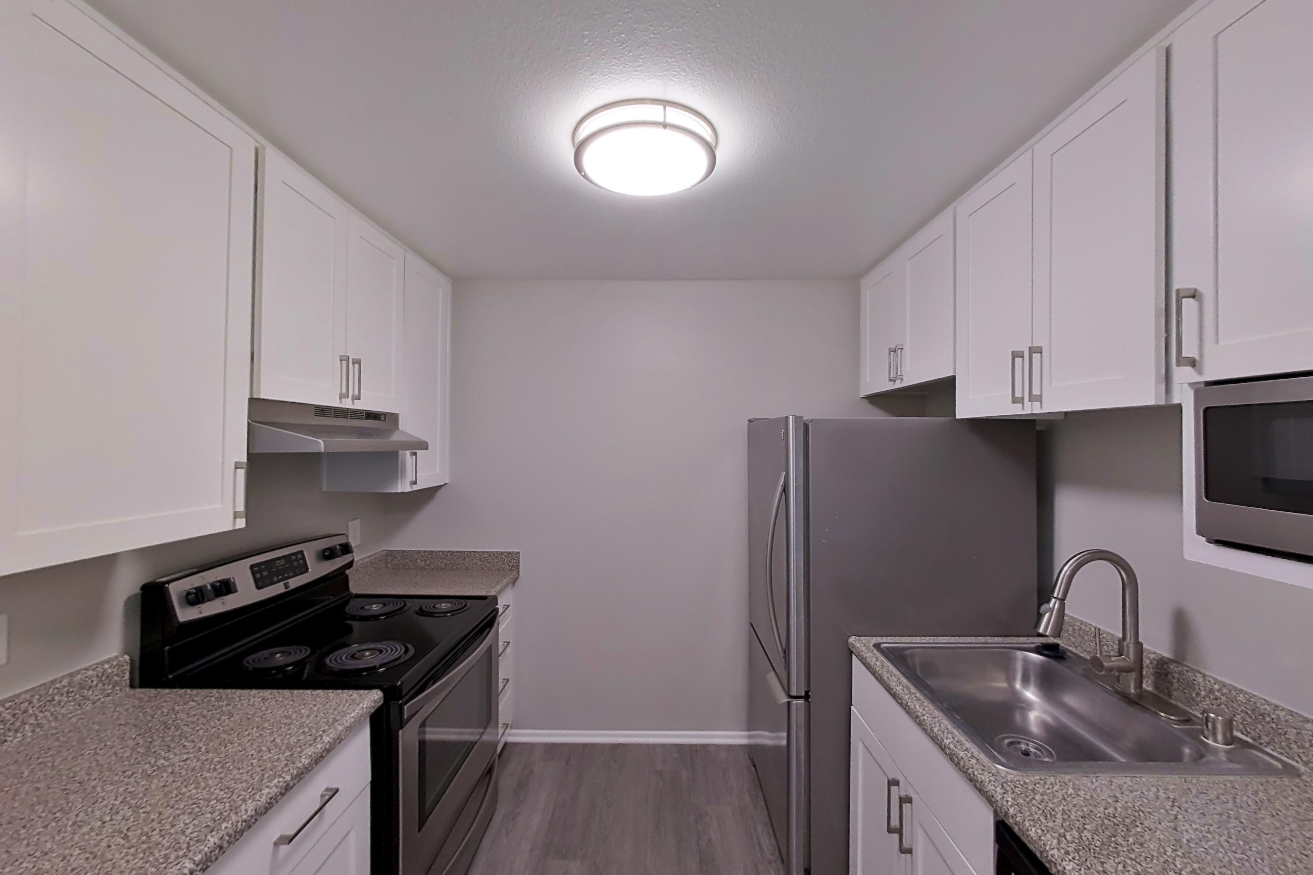 Kitchen with dark wood-finish flooring, dishwasher, electric range, light countertops, light stone countertops, microwave, oven/range, and stainless steel appliances, Apartment 11-08 at Avana Rancho Cucamonga