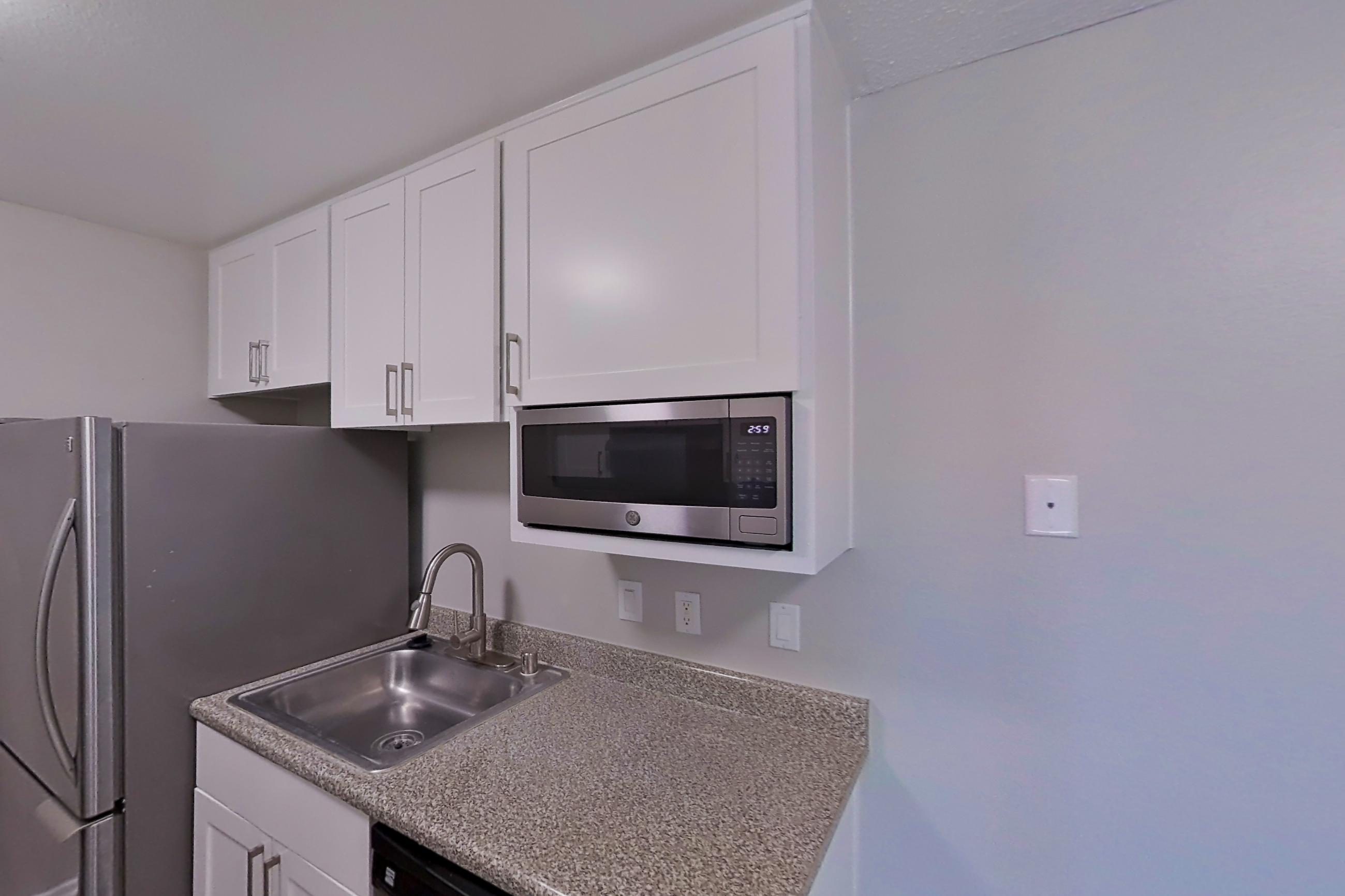 Kitchen with dark wood-finish flooring, dishwasher, electric range, light countertops, light stone countertops, microwave, oven/range, and stainless steel appliances, Apartment 11-08 at Avana Rancho Cucamonga