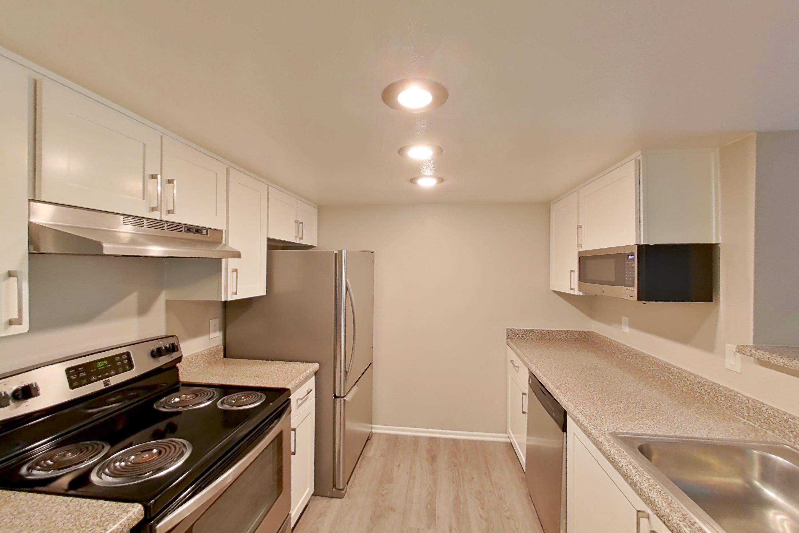 Kitchen with dishwasher, electric range, light countertops, light stone countertops, light wood-finish flooring, oven/range, refrigerator, and stainless steel appliances, Apartment 21 at Avana Rancho Cucamonga