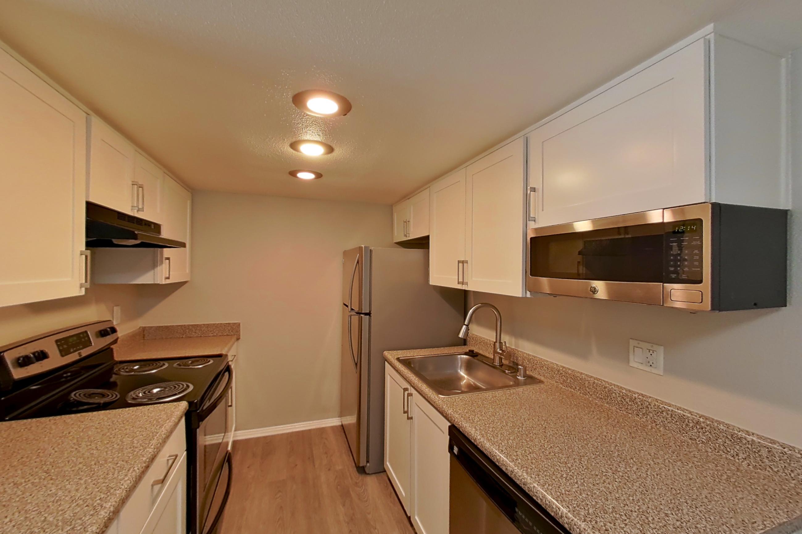 Kitchen with dishwasher, electric range, light countertops, light stone countertops, light wood-finish flooring, microwave, oven/range, range hood, refrigerator, stainless steel appliances, and white appliances, Apartment 08 at Avana Rancho Cucamonga