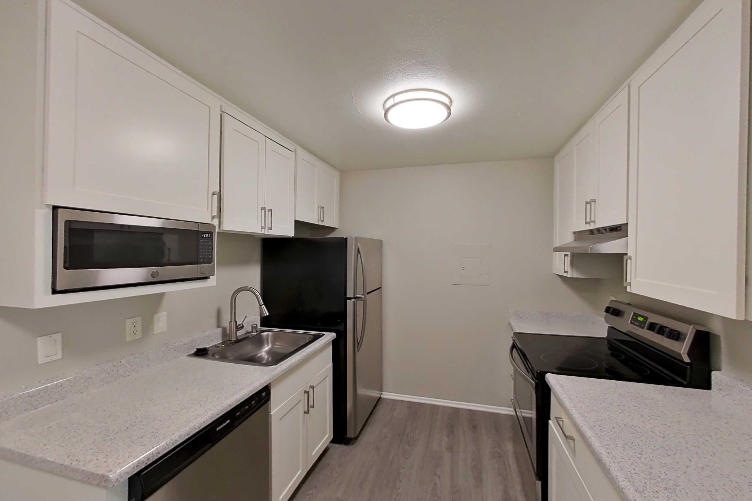 Kitchen with dishwasher, electric range, light stone countertops, light wood-finish flooring, oven/range, refrigerator, and stainless steel appliances, Apartment 12-10 at Avana Rancho Cucamonga