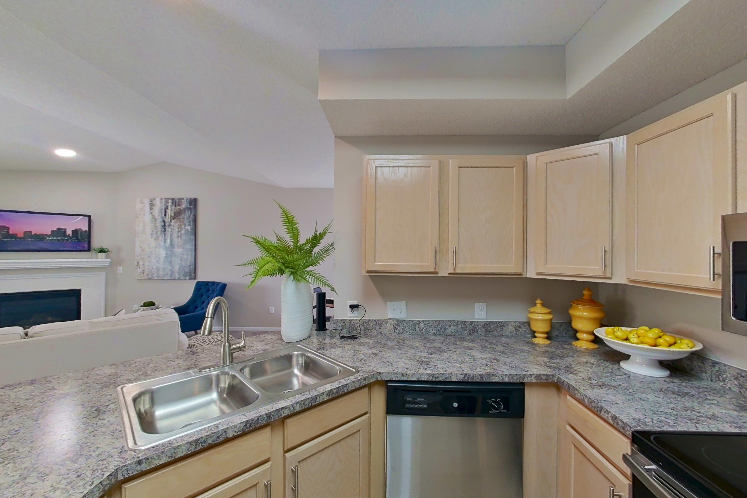 Kitchen with dishwasher, electric range, fireplace, light countertops, light stone countertops, light wood-finish flooring, microwave, oven/range, refrigerator, and stainless steel appliances, Apartment Bradford II at Bradford Pointe