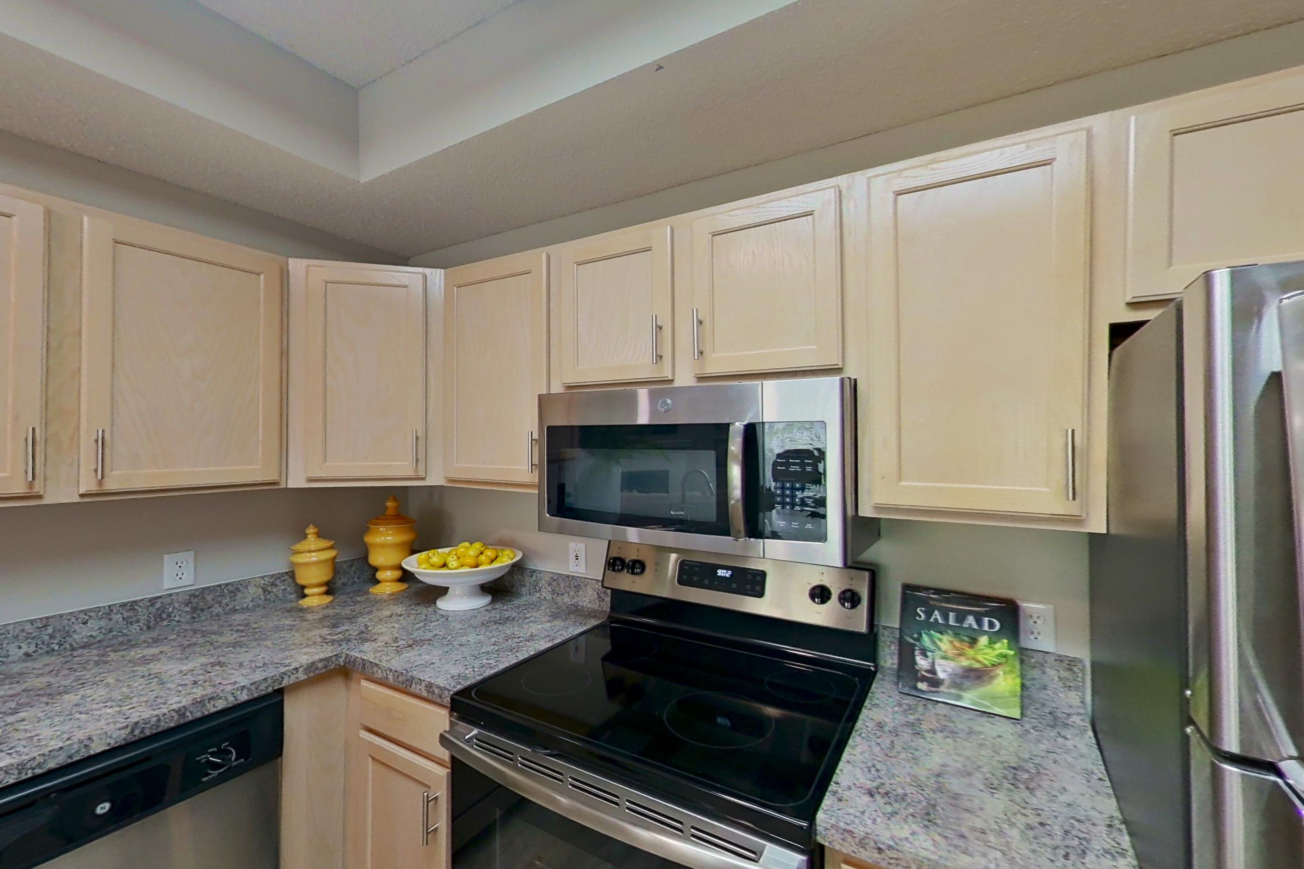 Kitchen with dishwasher, electric range, fireplace, light countertops, light stone countertops, light wood-finish flooring, microwave, oven/range, refrigerator, and stainless steel appliances, Apartment Bradford II at Bradford Pointe