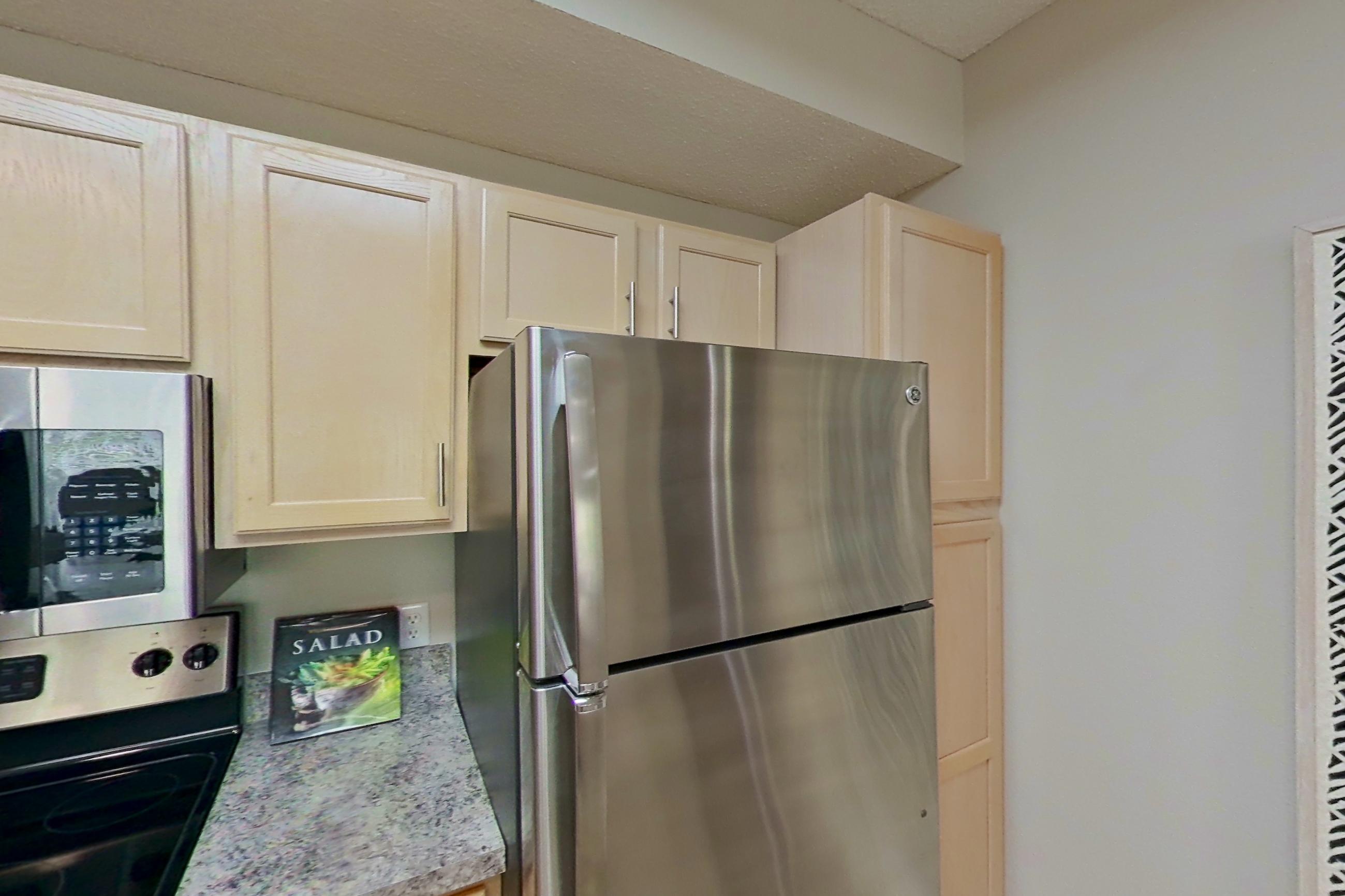 Kitchen with dishwasher, electric range, fireplace, light countertops, light stone countertops, light wood-finish flooring, microwave, oven/range, refrigerator, and stainless steel appliances, Apartment Bradford II at Bradford Pointe