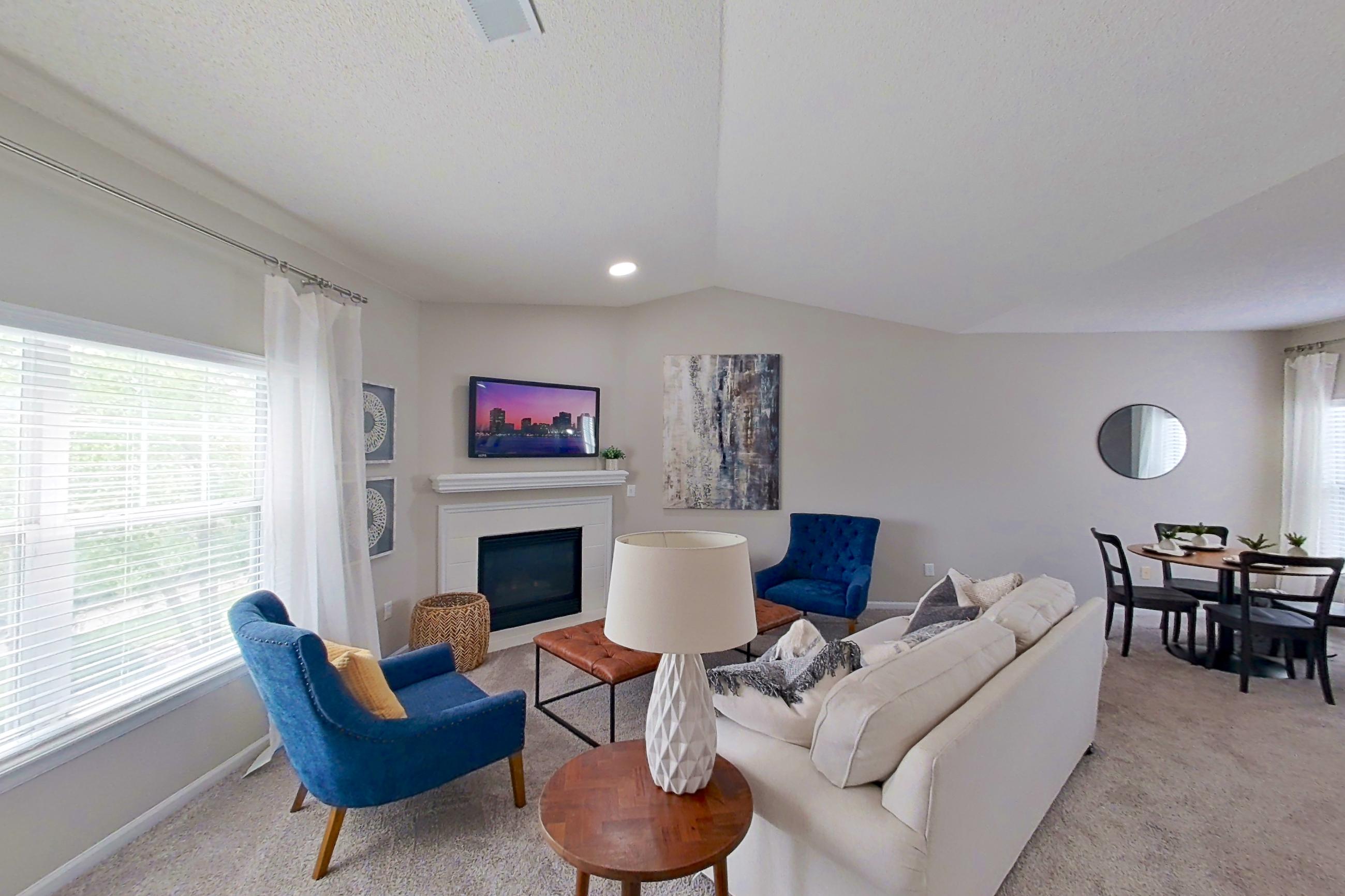 Living room with electric range, fireplace, light carpet, light countertops, light wood-finish flooring, oven/range, refrigerator, and stainless steel appliances, Apartment Bradford II at Bradford Pointe