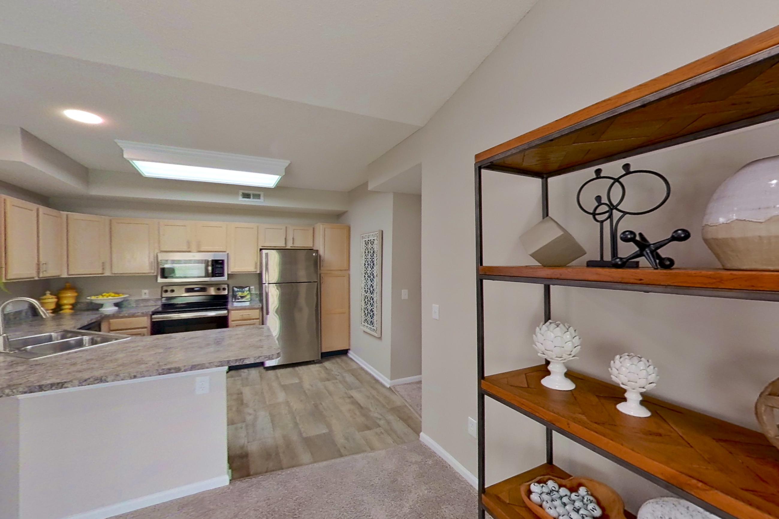 Living room with electric range, fireplace, light carpet, light countertops, light wood-finish flooring, oven/range, refrigerator, and stainless steel appliances, Apartment Bradford II at Bradford Pointe