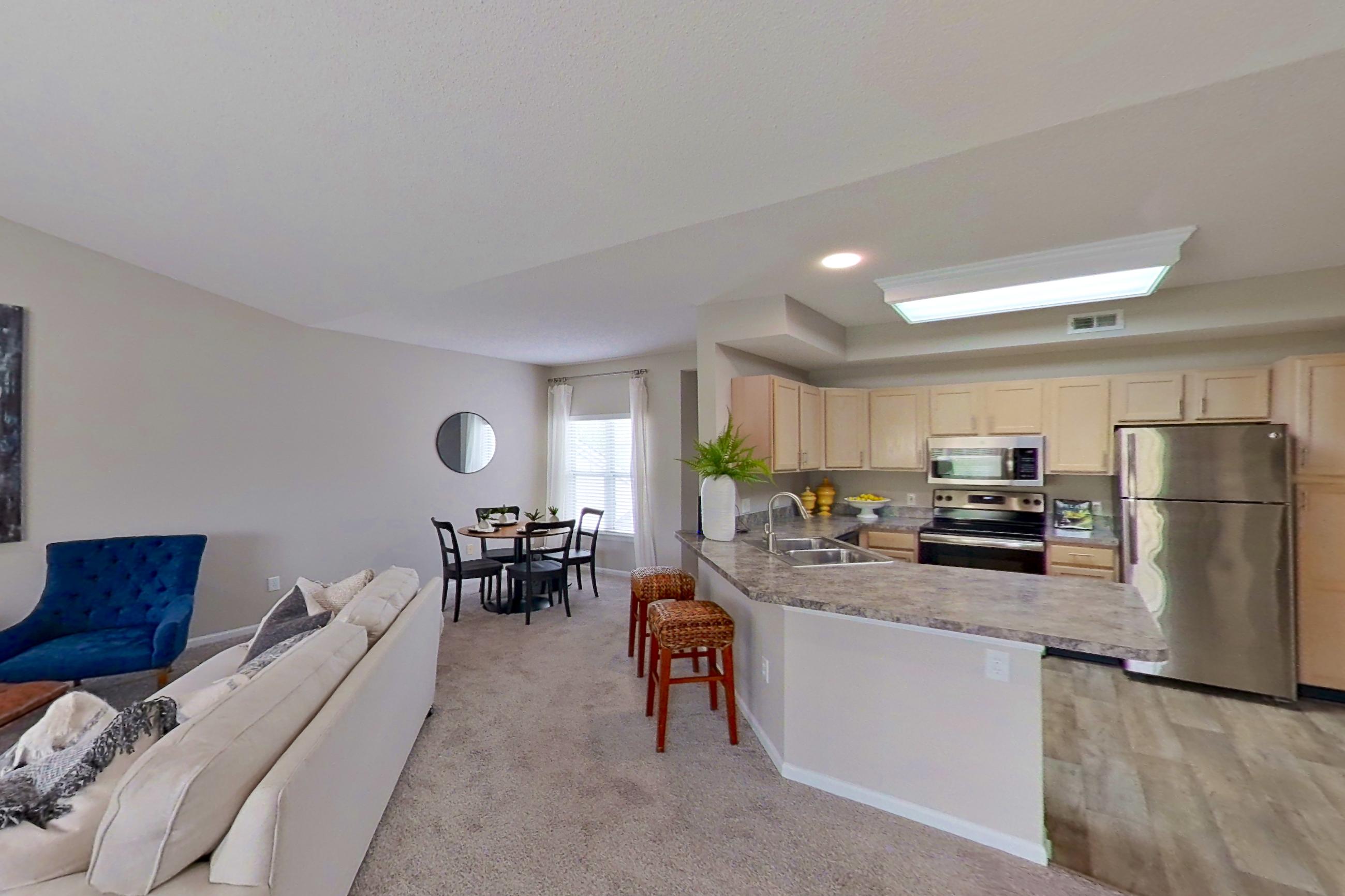 Living room with electric range, fireplace, light carpet, light countertops, light wood-finish flooring, oven/range, refrigerator, and stainless steel appliances, Apartment Bradford II at Bradford Pointe