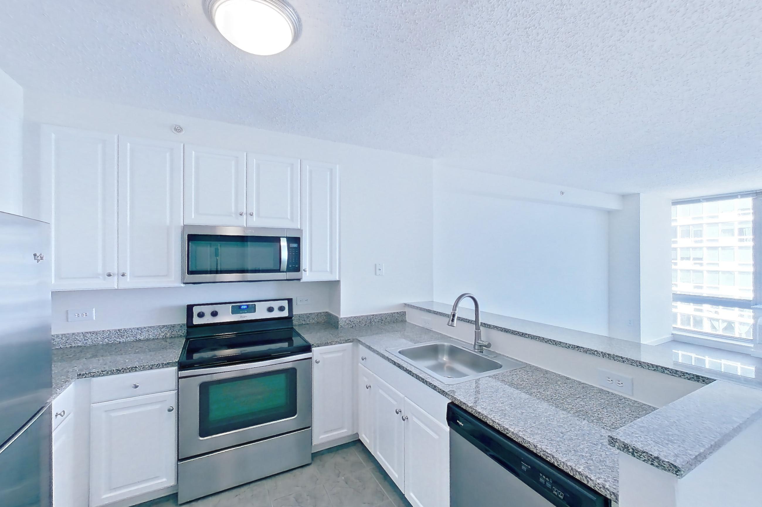 Kitchen with dark wood-finish flooring, dishwasher, electric range, light stone countertops, light wood-finish flooring, oven/range, refrigerator, and stainless steel appliances, Apartment LT-W2310 at Liberty Towers