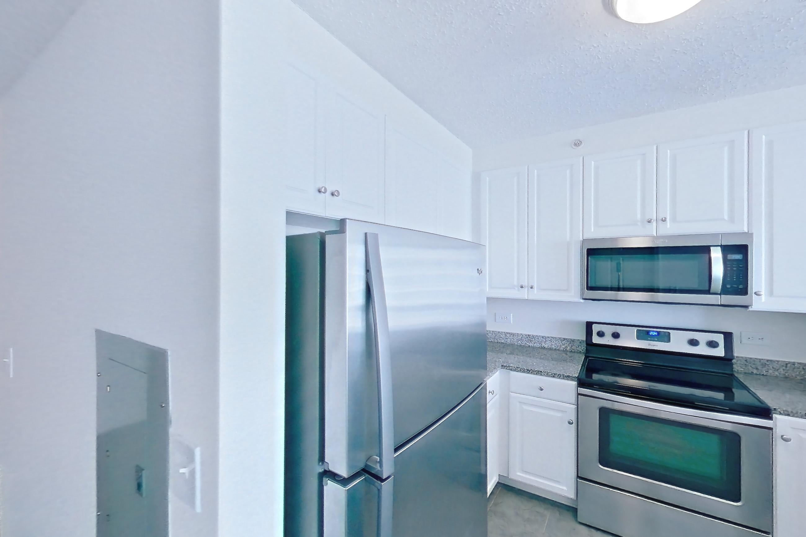 Kitchen with dark wood-finish flooring, dishwasher, electric range, light stone countertops, light wood-finish flooring, oven/range, refrigerator, and stainless steel appliances, Apartment LT-W2310 at Liberty Towers