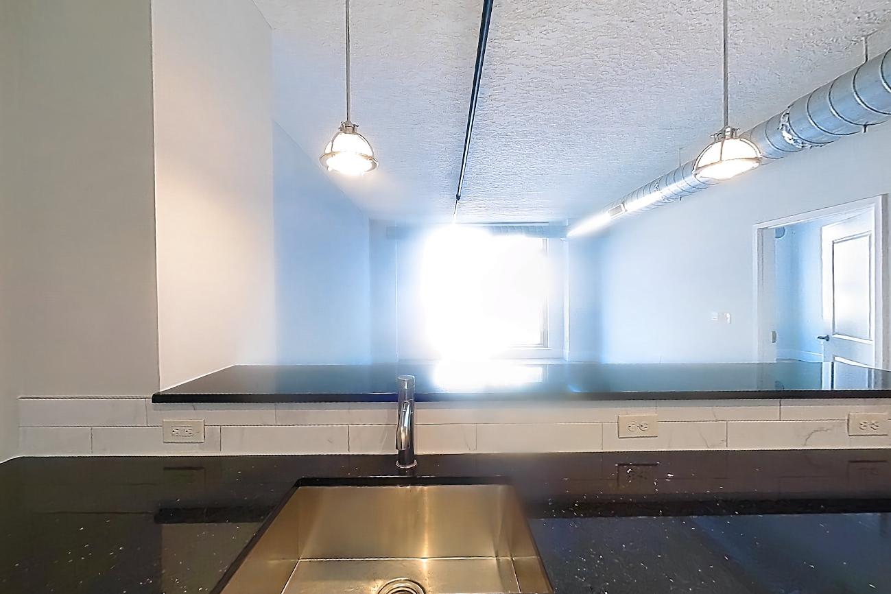 Kitchen with dark stone countertops, dishwasher, electric range, light wood-finish flooring, oven/range, range hood, refrigerator, stainless steel appliances, and water & ice dispenser, Apartment SL-0732 at Soho Lofts