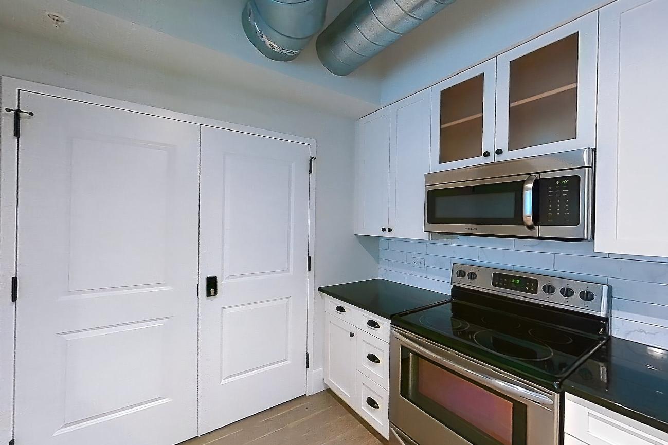 Kitchen with dark countertops, dark stone countertops, dishwasher, electric range, light wood-finish flooring, oven/range, and stainless steel appliances, Apartment SL-1001 at Soho Lofts