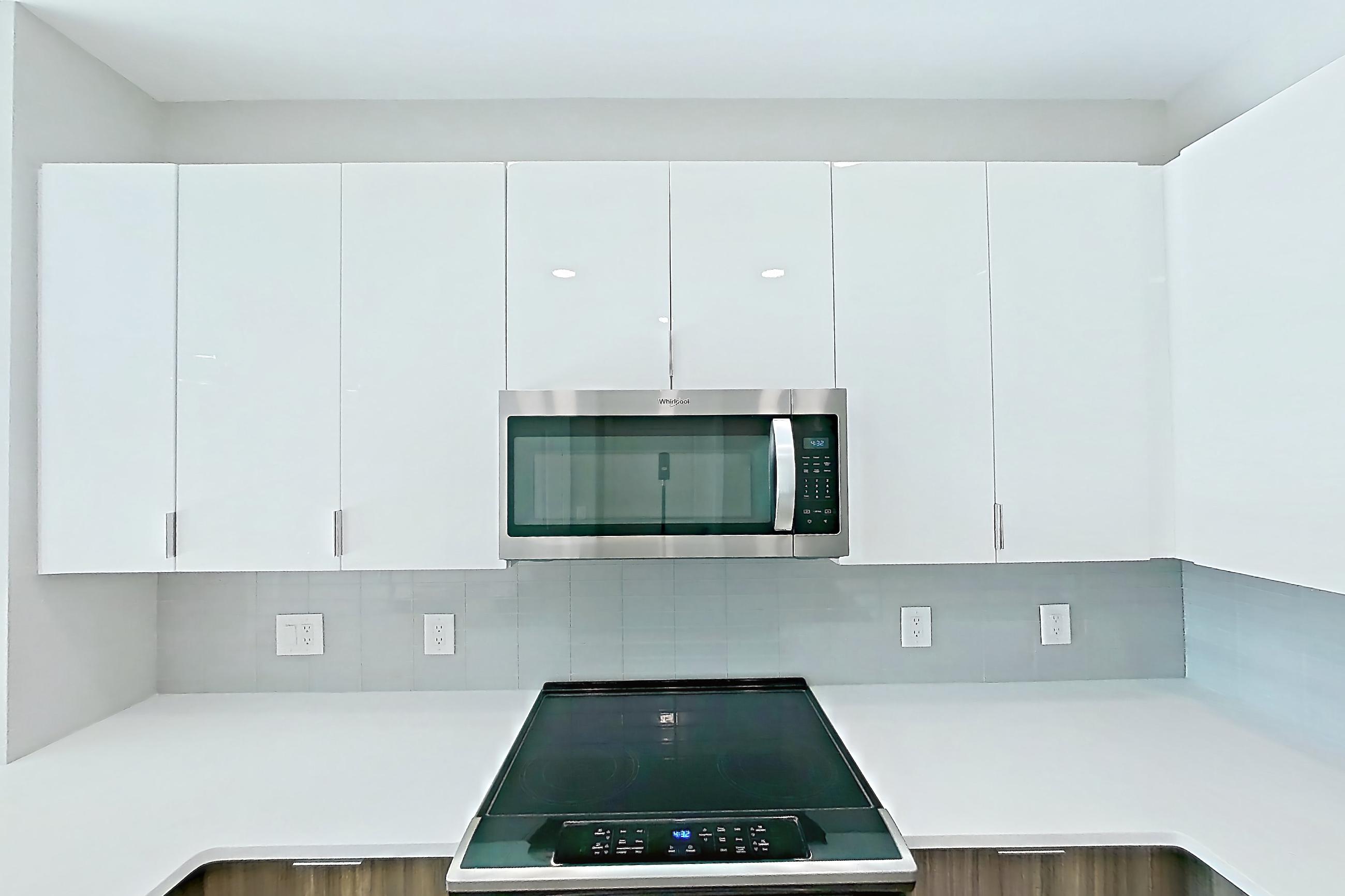 Kitchen with dishwasher, electric range, light countertops, light stone countertops, light wood-finish flooring, microwave, oven/range, and stainless steel appliances, Apartment EM-7513 at The Emery at Overlook Ridge