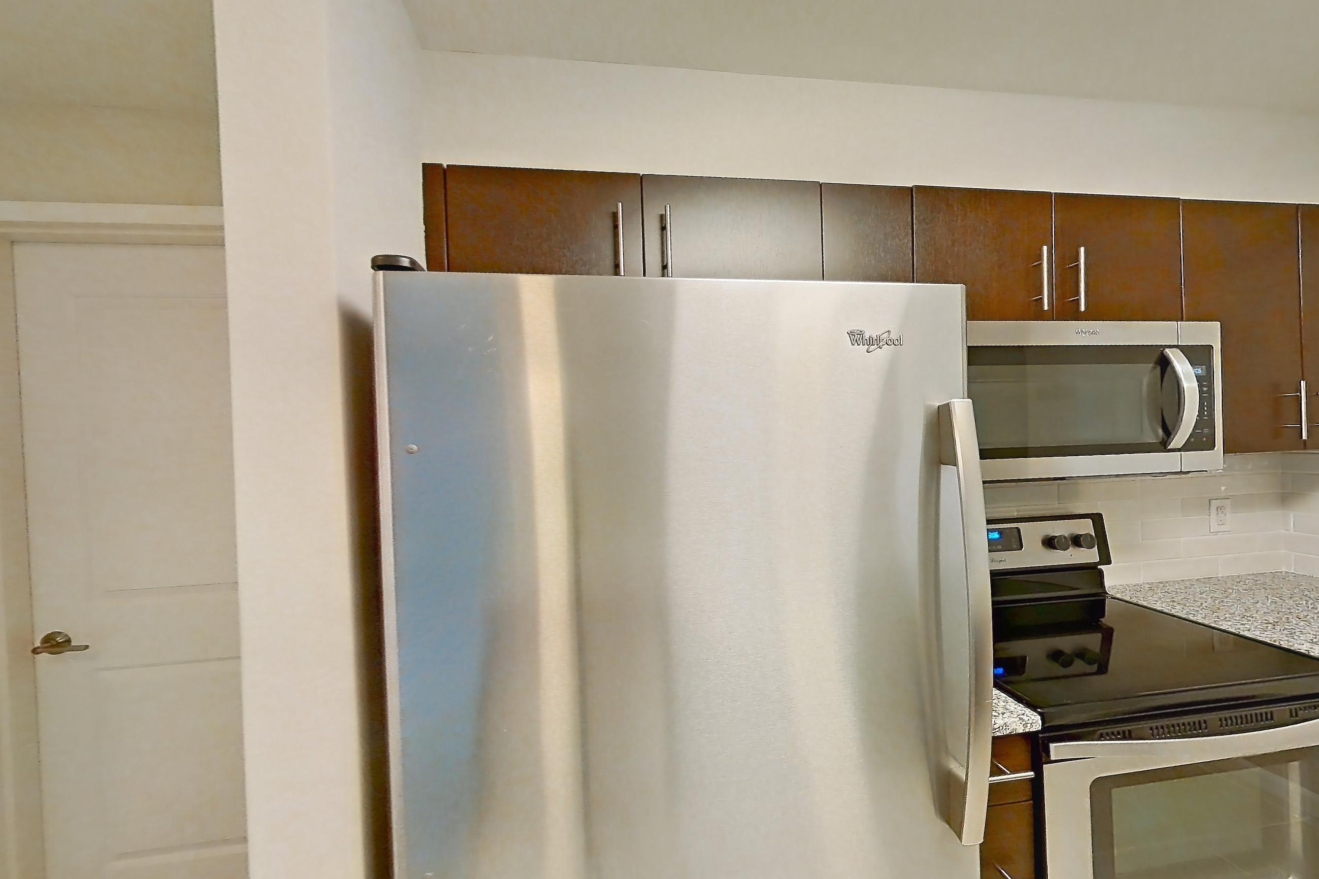 Kitchen with dishwasher, electric range, light countertops, light stone countertops, light tile flooring, light wood-finish flooring, microwave, oven/range, refrigerator, stainless steel appliances, and white appliances, Apartment RT-0615 at RiverTrace at Port Imperial
